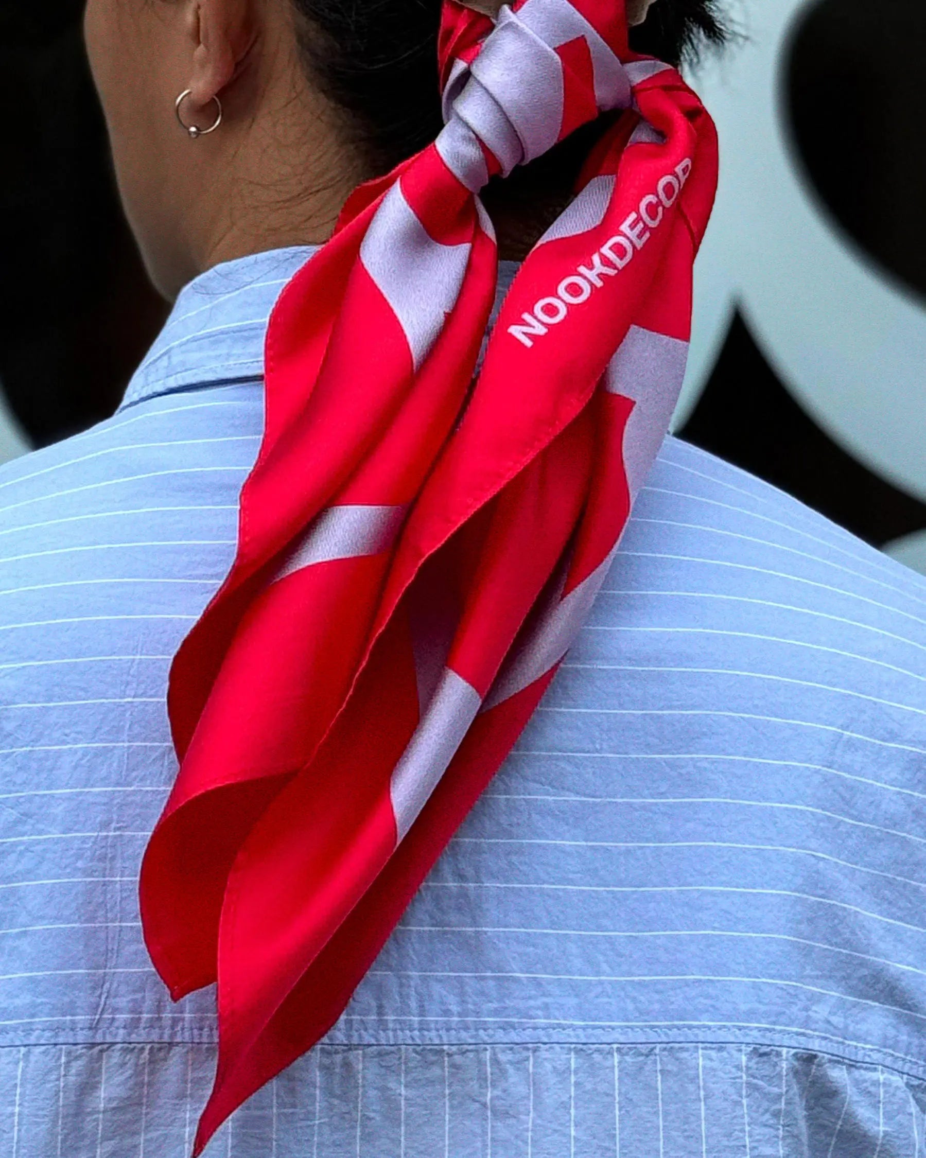 Dopamine red and purple silk scarf, handkerchief with NOOKDECOR logo design tightened on behind the cap on a man and he's wearing a light blue shirt.