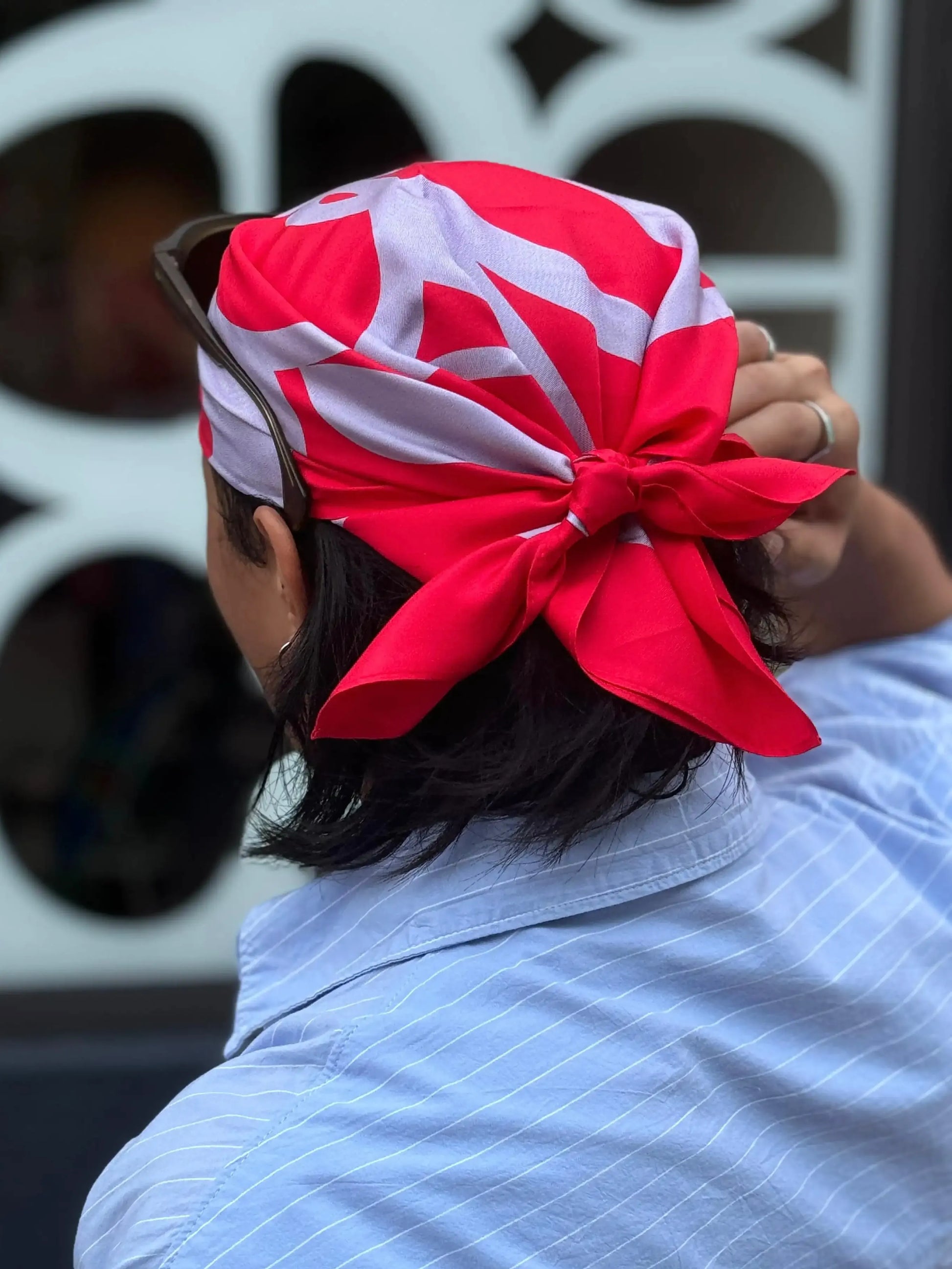 A man wearing a colorful red and pastel purple bandana with geometric NOOKDECOR's logo with a light blue shirt and a blurred background.