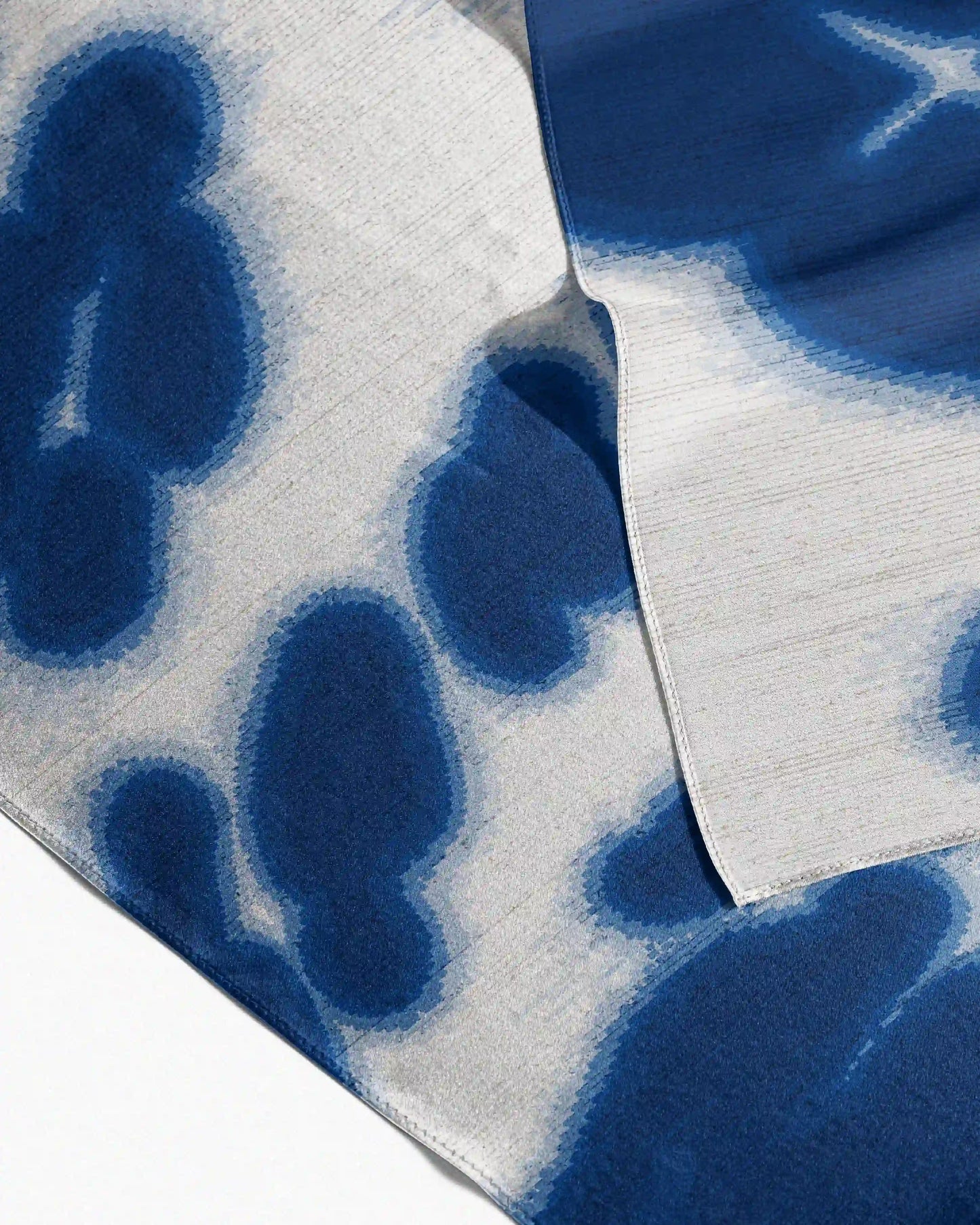 Close-up of a silk handkerchief with Klein blue and off-white, with abstract floral and leopard pattern, placed on a beige background, a dopamine fashionable accessory for eclectic style.
