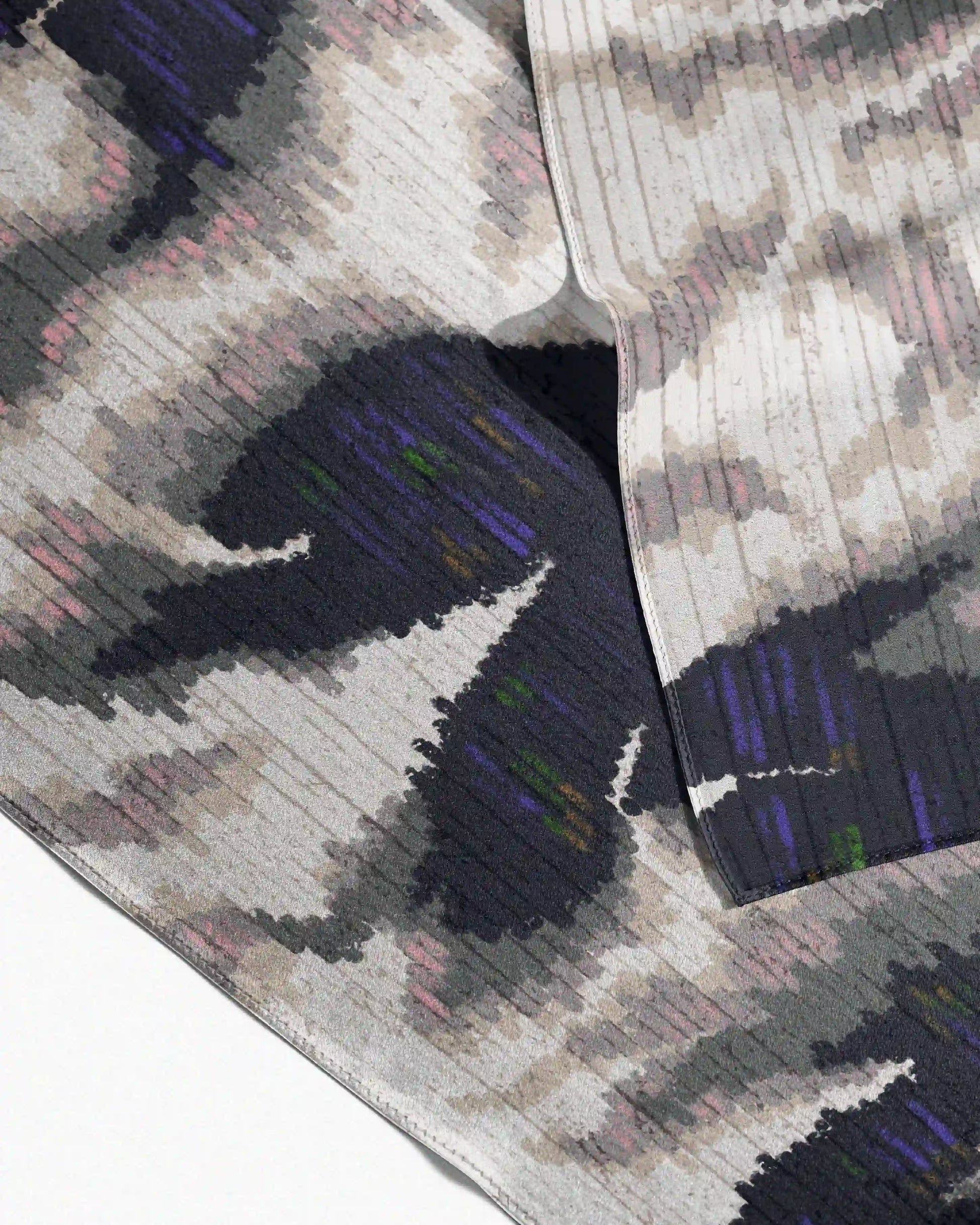 A luxurious 100% mulberry silk scarf arranged to show its abstract fish and floral pattern and edge binding detail.