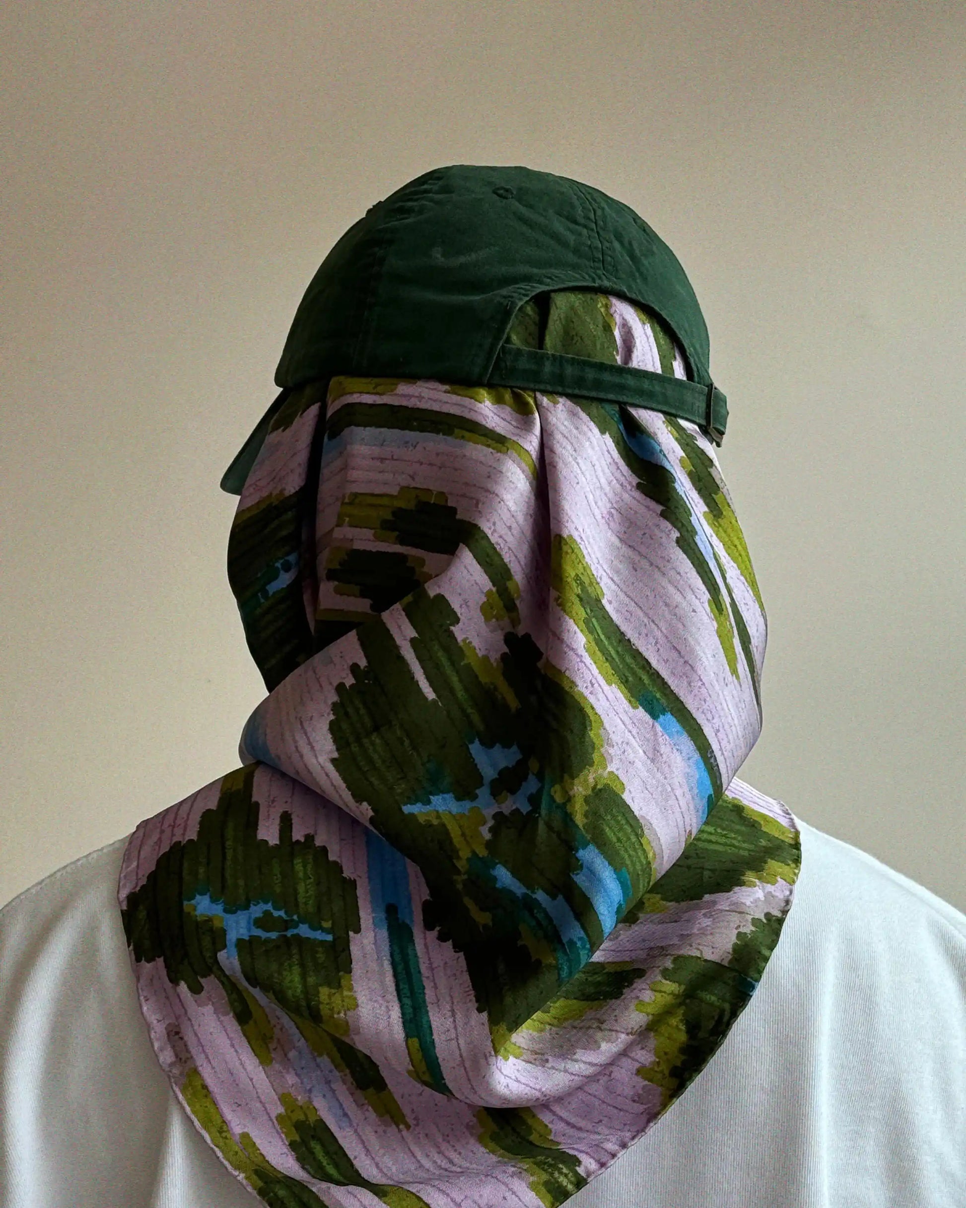 Man wearing a dopamine green cap and purple abstract leopard patterned silk bandana with a touch of green and blue hues, easily match with white top, front of a plain background.