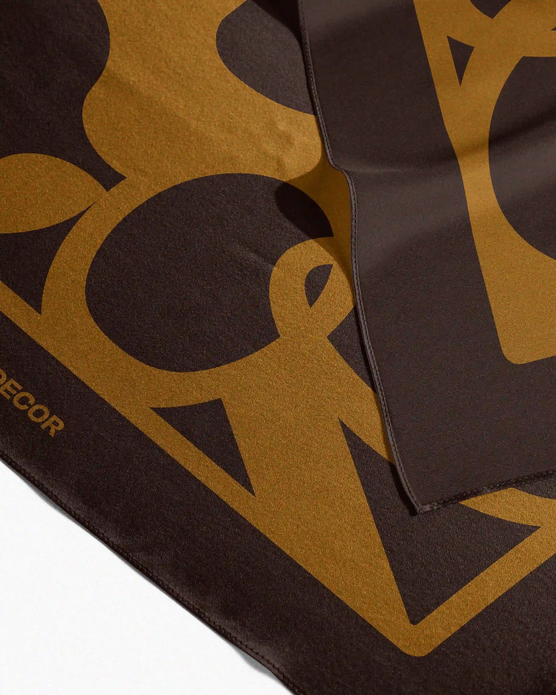 This versatile golden mustard yellow and brown mulberry silk scarf is neatly folded on a beige background, showcasing its precise edge binding, perfect for use as a sophisticated waist scarf, bandana, handkerchief, twilly, or placemat.