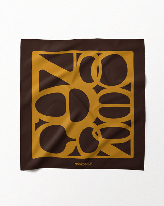A mustard yellow and dark brown handkerchief, 100% mulberry silk bandana features geometrical design of NOOKDECOR’s brand logo, laid flat on a beige background, showcasing its eclectic style.