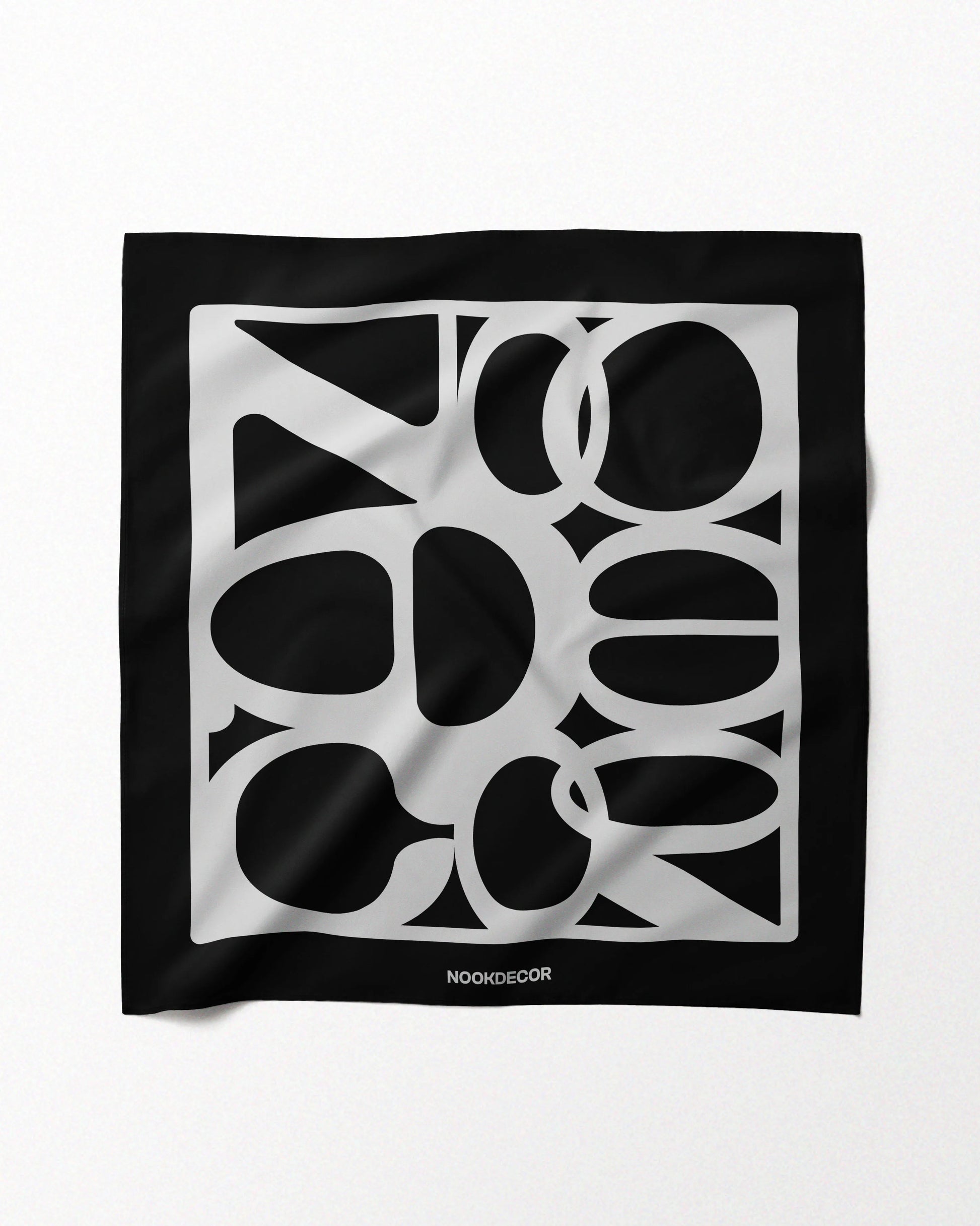 A classic black and white handkerchief features NOOKDECOR’s brand logo design and is made with 100% mulberry silk, laid flat on a beige background, showcasing its eclectic style.