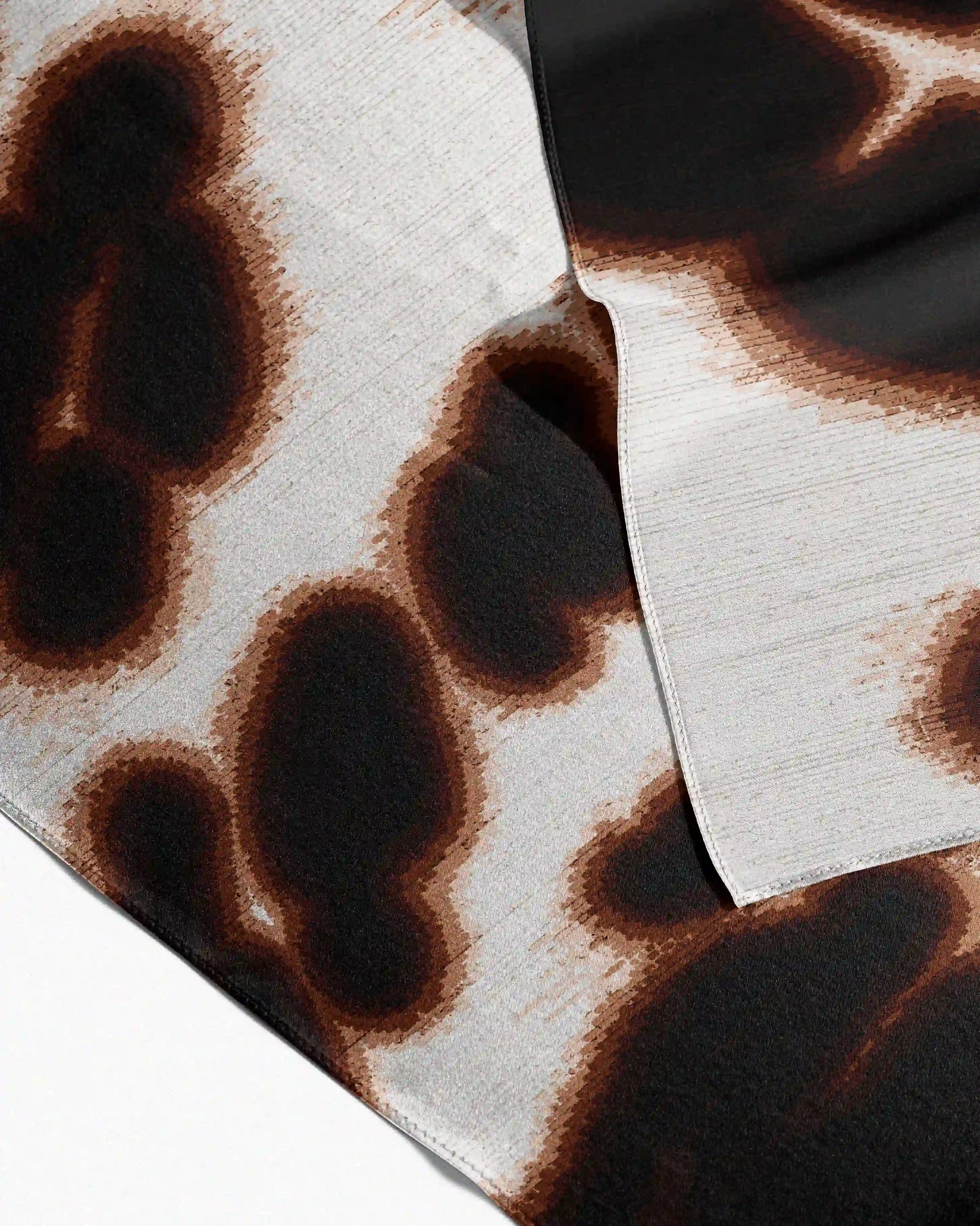Close-up of a 100% mulberry silk bandana  features a brown and cream white abstract floral and leopard pattern, with the edge binding detail, placed on beige background, for eclectic and maximalist style lover.