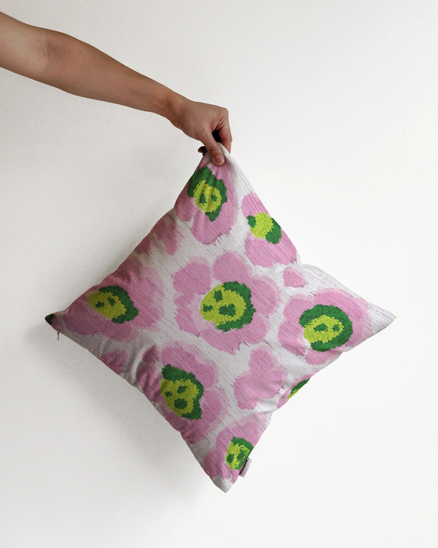 A hand holding a bold abstract floral and leopard cushion cover in pink, green and off white hues, against a minimalist beige background, perfect for eclectic dopamine decor in a maximalist modern apartment.