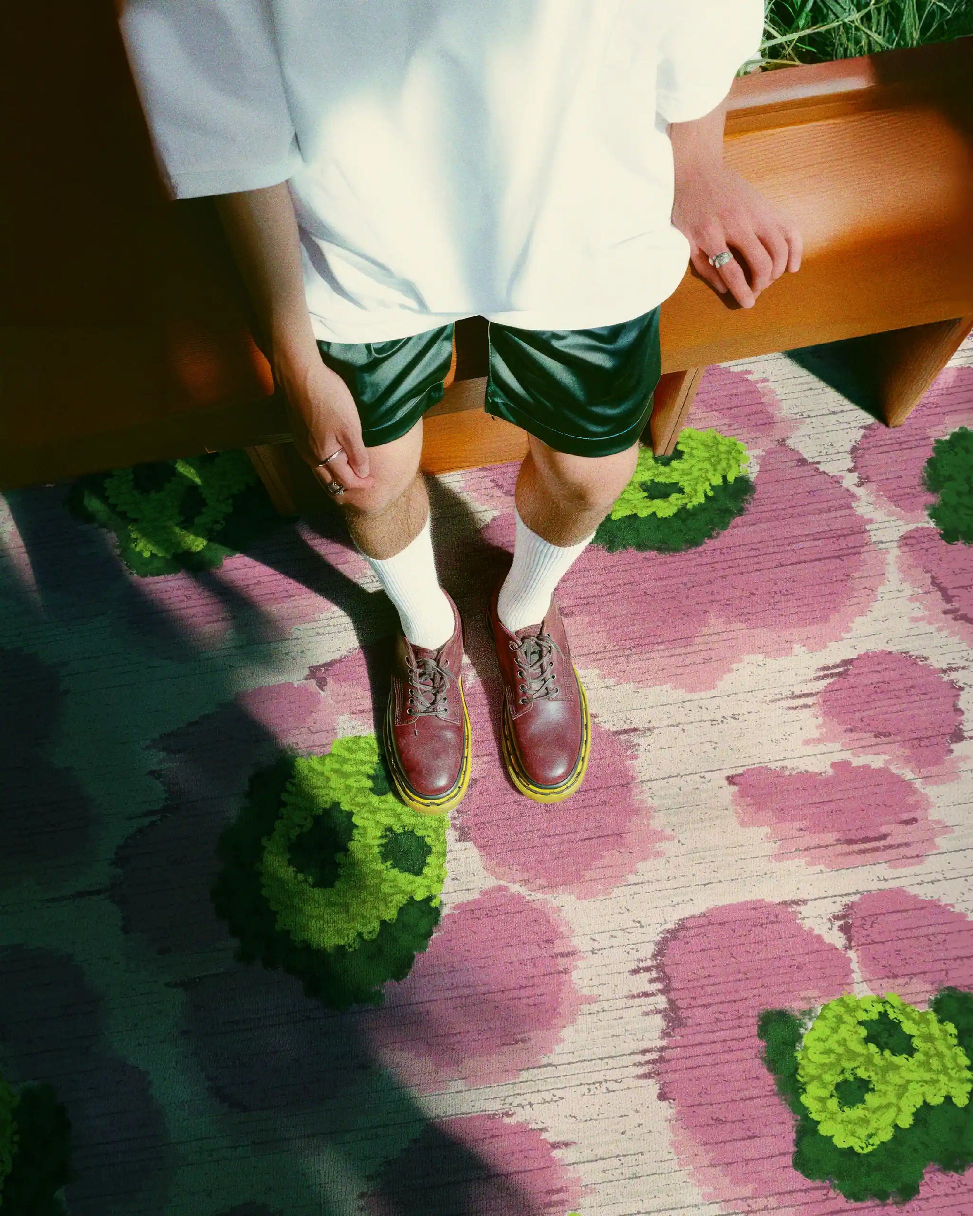 A man wearing a white tee and dark green shorts stands on the eclectic floral area rug with cute leopard designs in pink and green hues in a cozy living room.