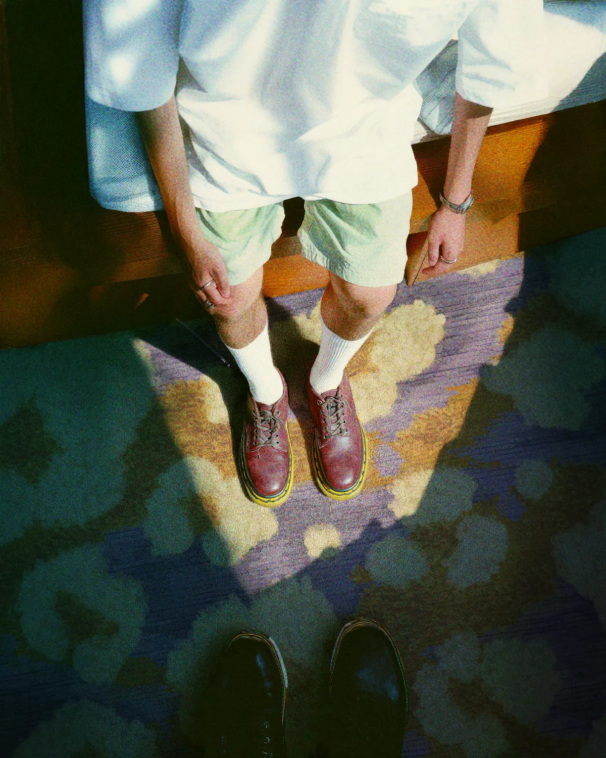 A man wearing a white tee and mint shorts stands on the colorful area rug in purple and yellow hues designed for maximalist home decor lovers.