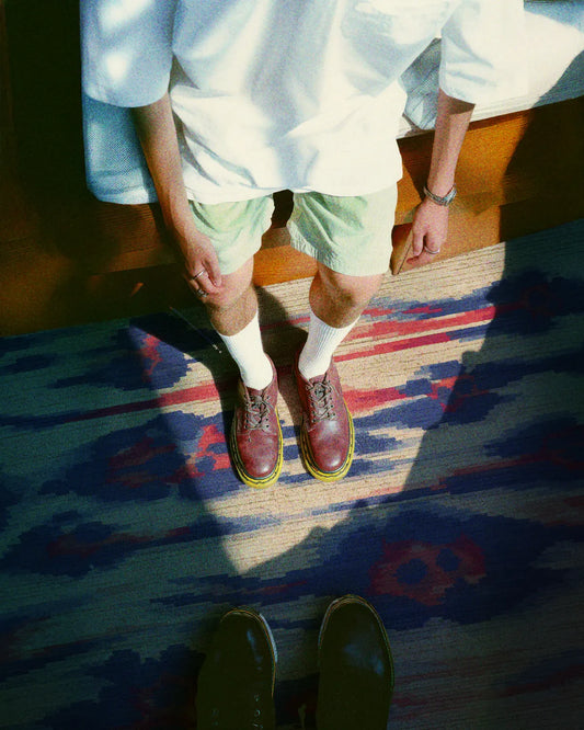 A man stands on an eclectic beige, blue, and coral colored area rug, wearing a trendy summer outfit in his modern living room.