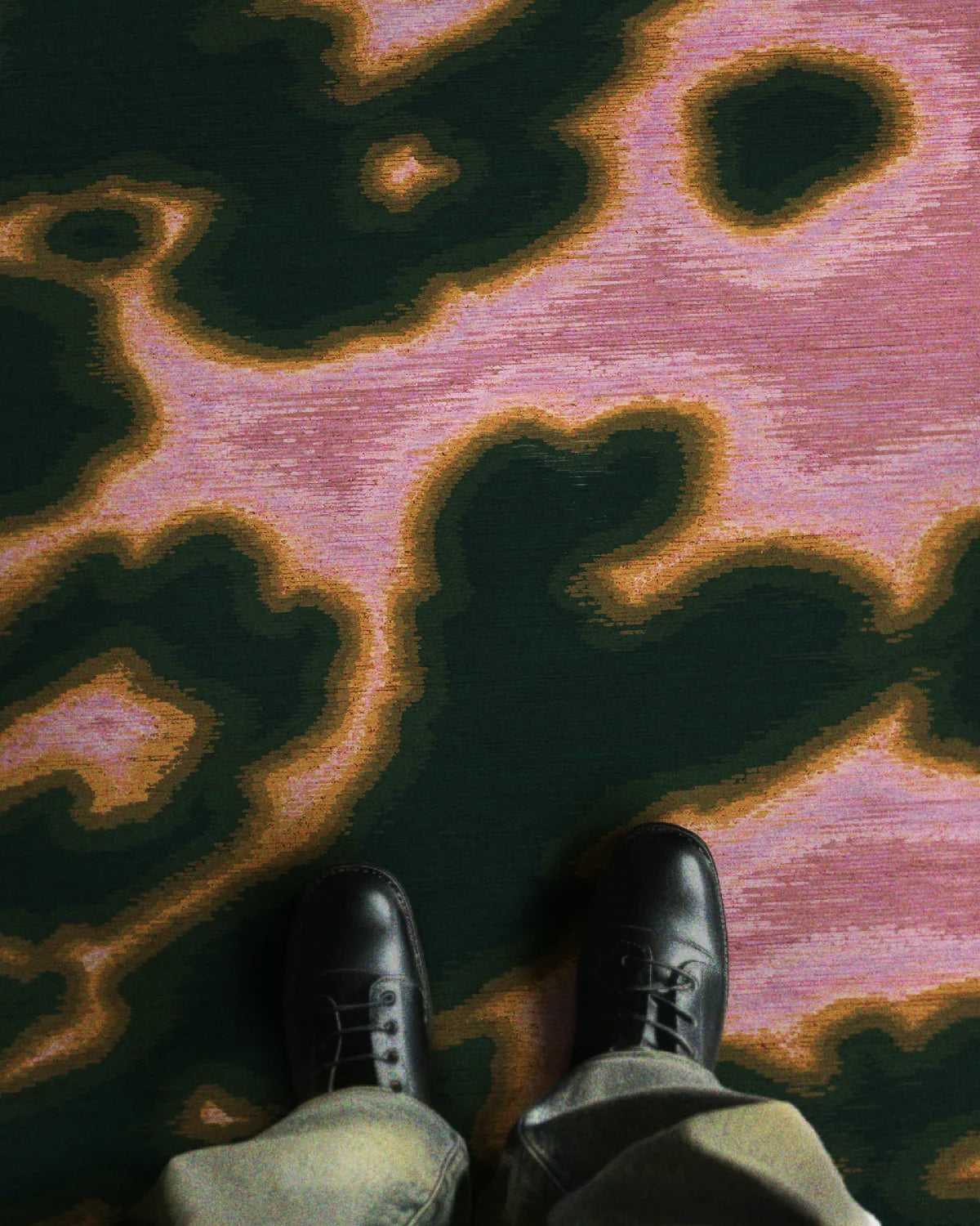 A man in trendy baggy jeans and black leather shoes stands on a faux cowhide rug featuring abstract floral patterns in hot pink and dark green hues, radiating a contemporary vibe in a stylish setting.