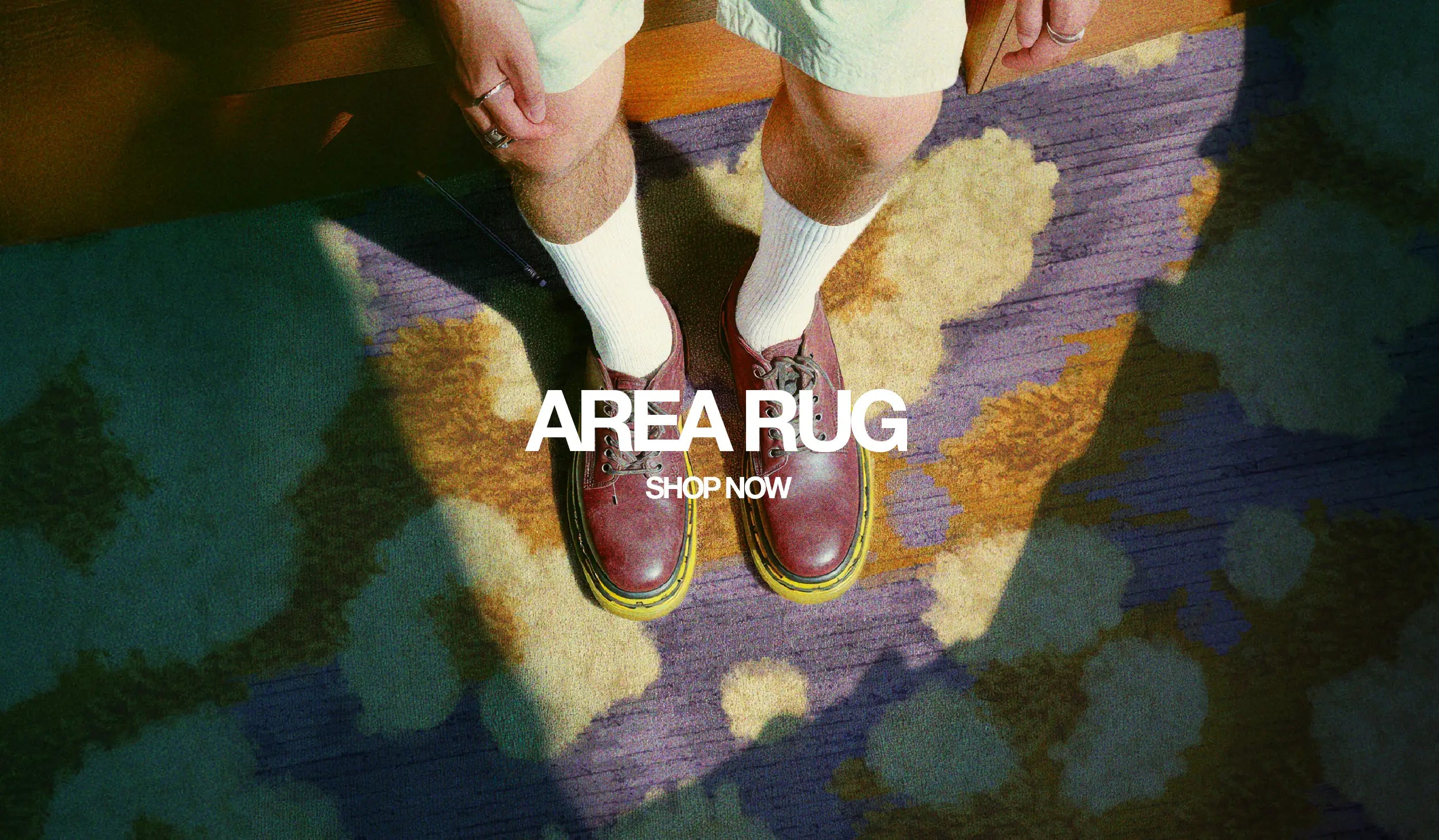 A banner for the rug collection displays two men standing on an eclectic area rug with shades of purple and yellow in a living room.