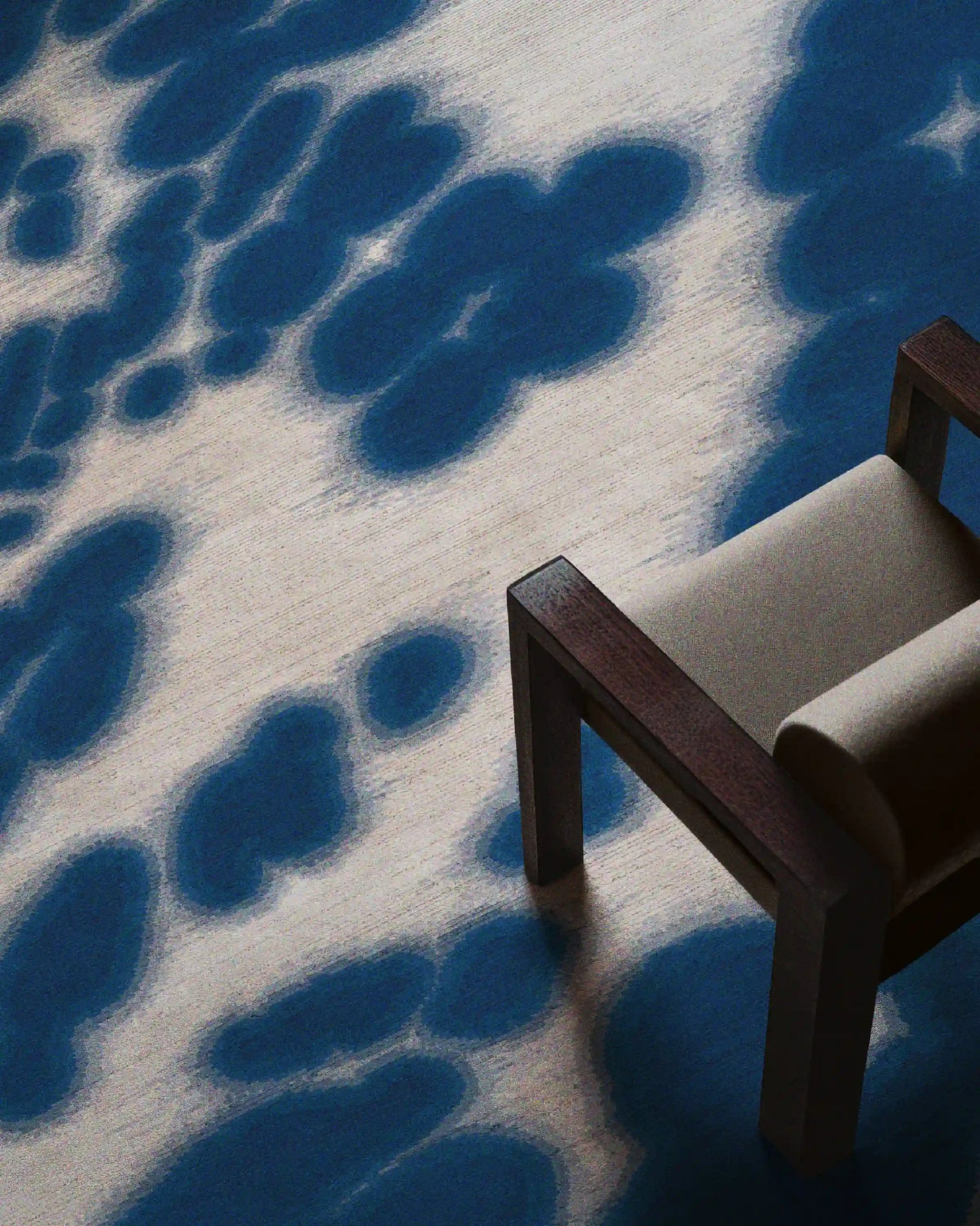 Floral cowhide rug in Klein blue and off white aura area rug placed underneath a light grey wood armchair in the living room.
