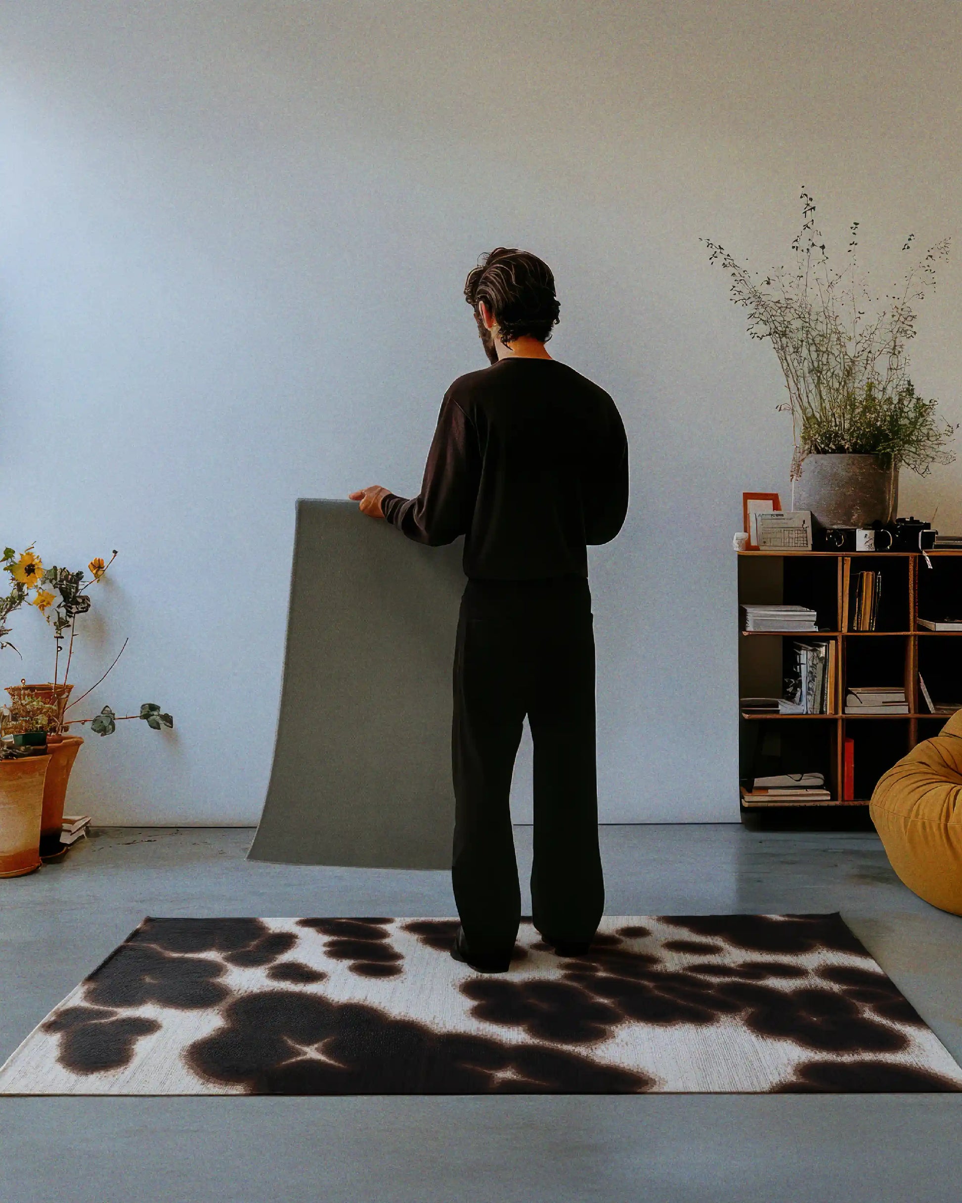 A man holding and showing the back of the rug with a slip-resistant backing, showcasing it in a living room, standing on a dark brown floral cowhide area rug for the maximalist eclectic home.