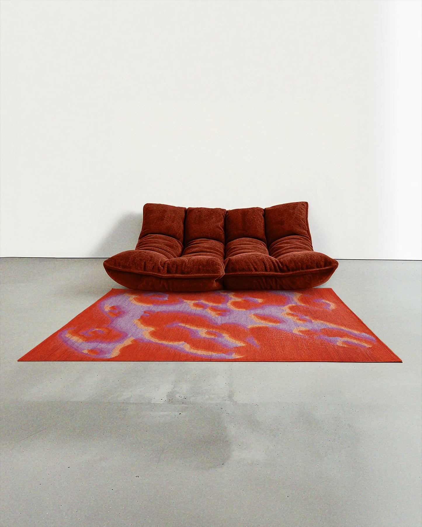 A dopamine abstract camouflage area rug measuring 5ft by 7ft, in orange, red, and pastel purple tones, placed in a contemporary modern studio with a dark rusty orange two-seat sofa.
