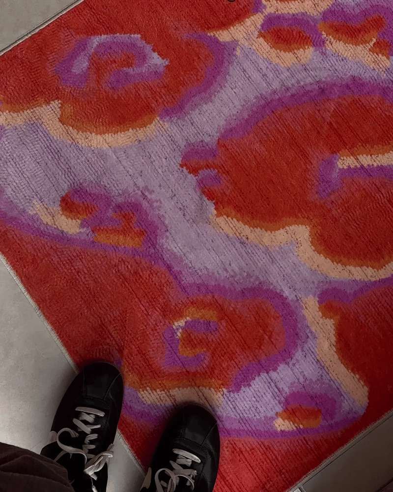 Colorful patterned rug with red and purple design, feet wearing black shoes at the bottom.