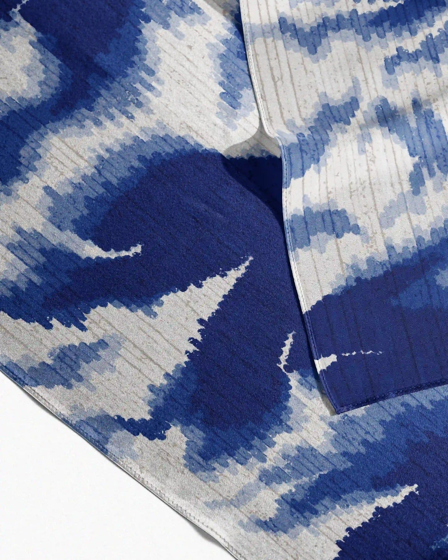Close-up on the abstract fish design, maximalist floral pattern of this versatile Klein blue and off white mulberry silk scarf.