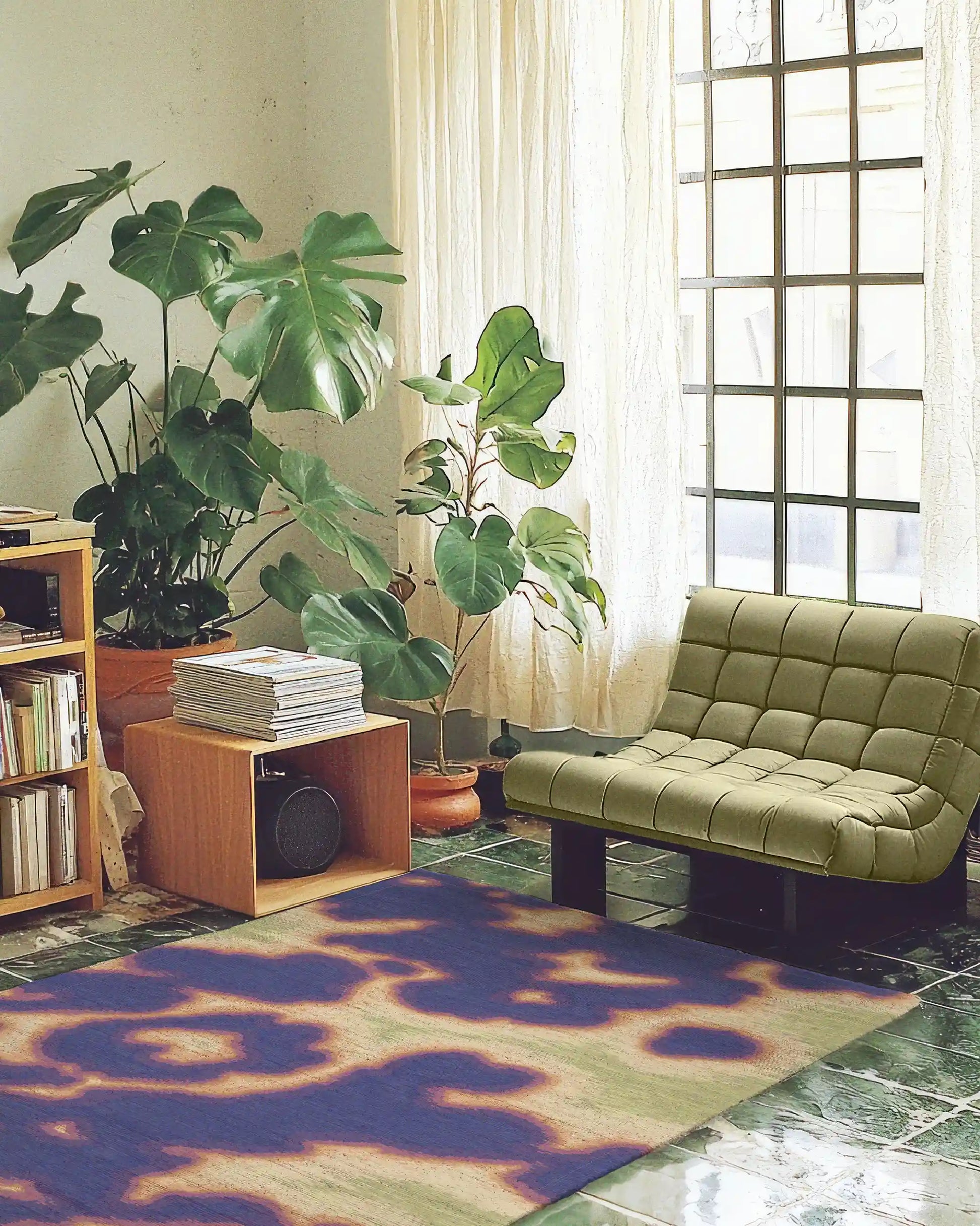 An eclectic abstract cowhide floral area rug is placed in a cool and cozy apartment, featuring books in cabinets, large houseplants, and sage green single sofa on green tiled floor. This rug showcases hand painted cowhide and floral patterns, embodying an aura and psychedelic style with vivid hues of purple, yellow, orange, and green. Perfect for dopamine home decor and aesthetic decor lovers.