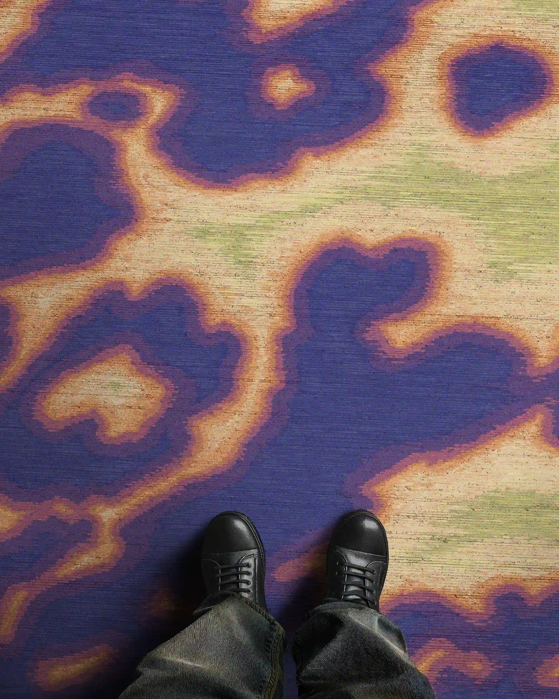 Man standing on an eclectic home decor, the dopamine colorful purple psychedelic area rug, with hand painted abstract cowhide animal print design with faux textile texture in vivid purple, orange, yellow and green hues printed faux wool low pile area rug 8x10 ft.