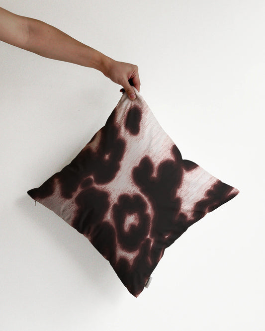 A hand holding a bold abstract cowhide and floral cushion cover in brown and off white against a minimalist beige background, perfect for eclectic dopamine decor in a modern apartment.
