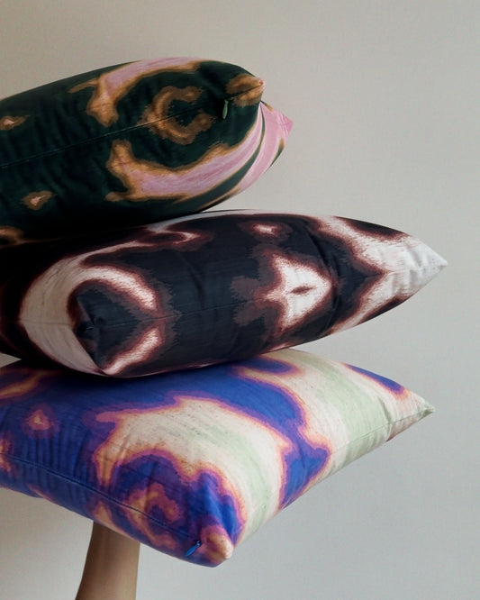 Set of 3 coordinating throw pillows in dopamine colorful cushion covers held against beige white wall, showing mix of abstract floral cowhide for bold and eclectic sofa styling. Including, Pink and dark green/ Purplish blue and light green and dark brown and off white.