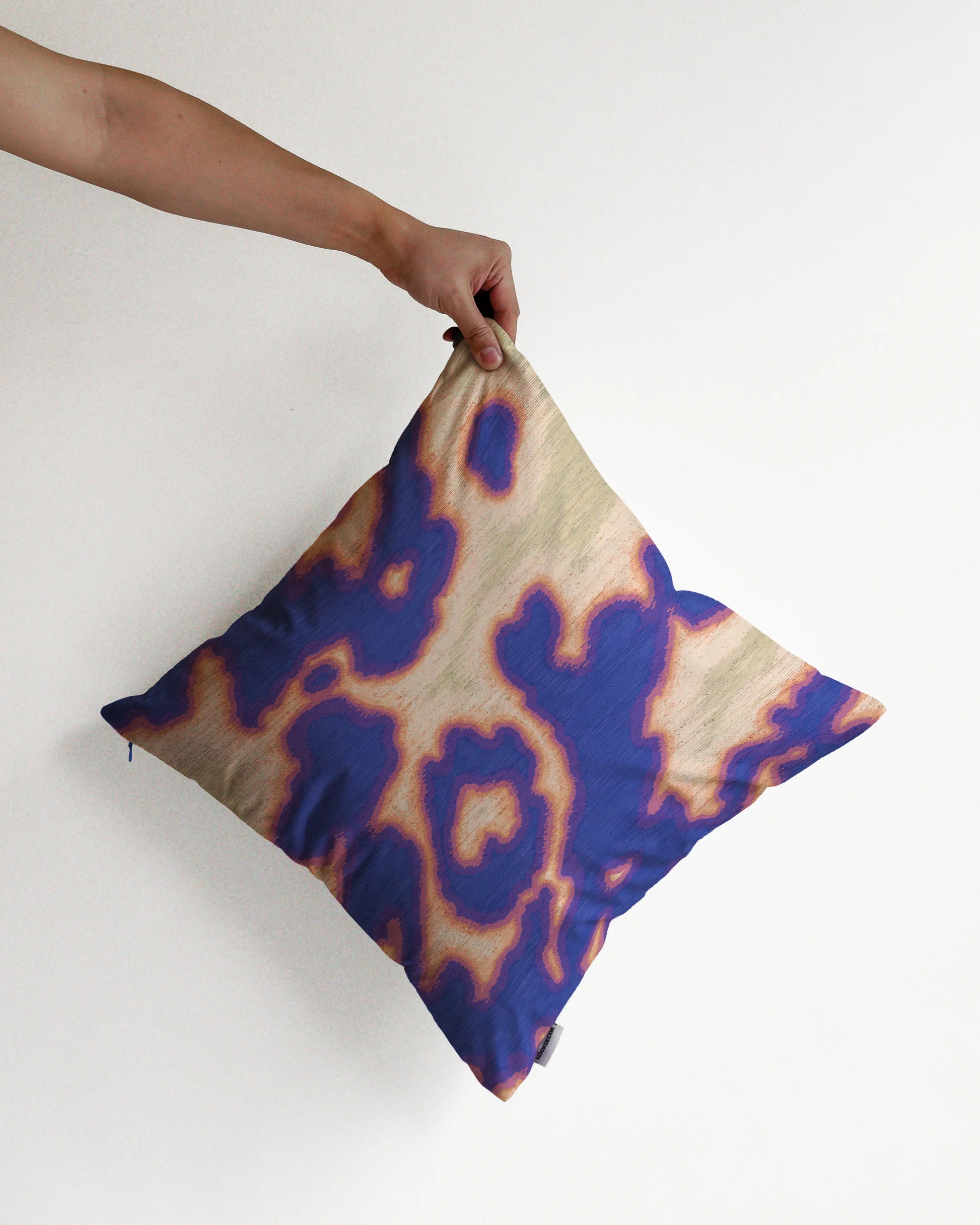 A hand holding a bold abstract cowhide and floral cushion cover in purplish blue, light green and yellow hues, against a minimalist beige background, perfect for eclectic dopamine decor in a modern apartment.