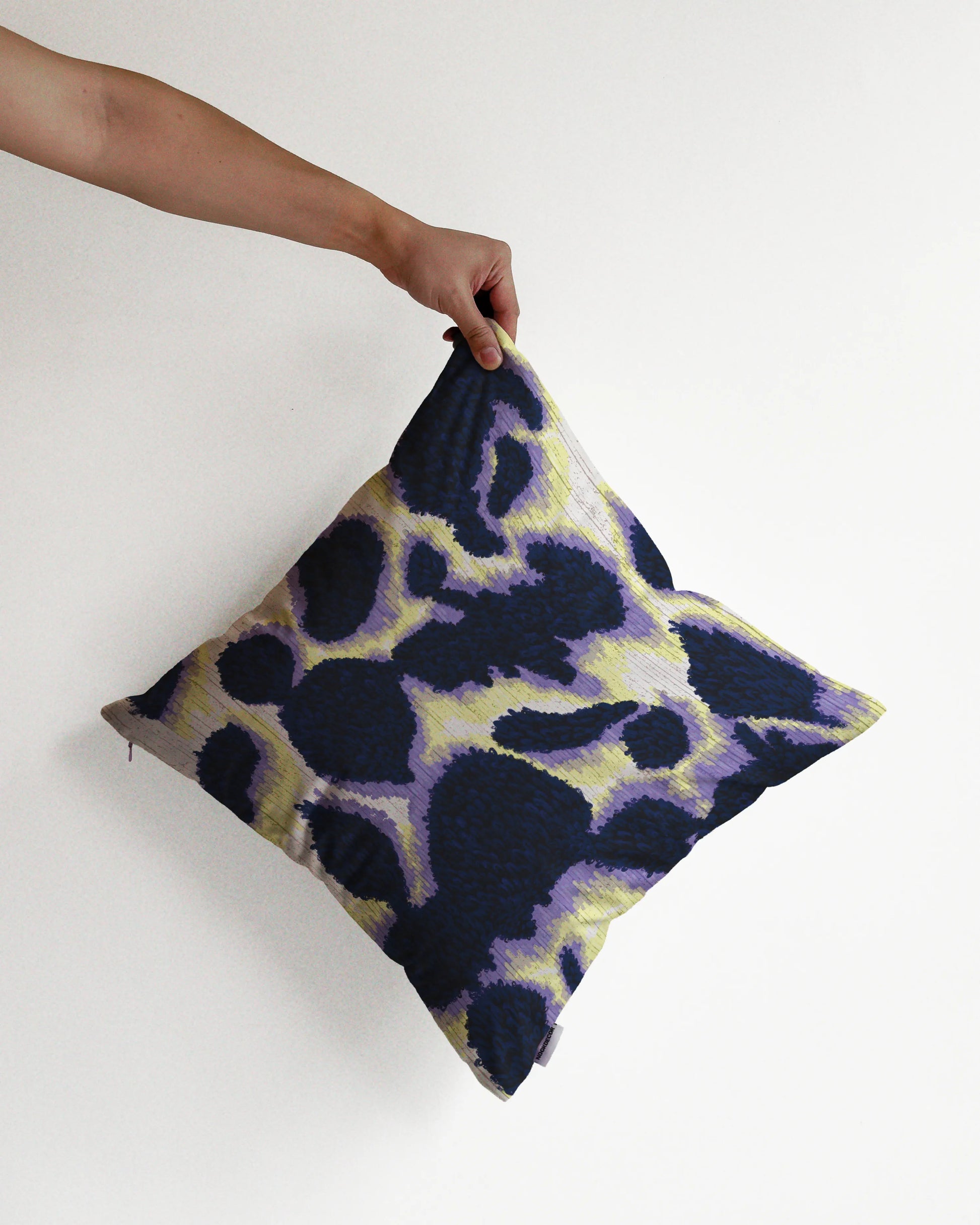 A hand holding a bold abstract cowhide cushion cover in dark blue, pastel pueple and off white hues, with a slight touch of light yellow, against a minimalist beige background, perfect for eclectic dopamine decor in a modern apartment.
