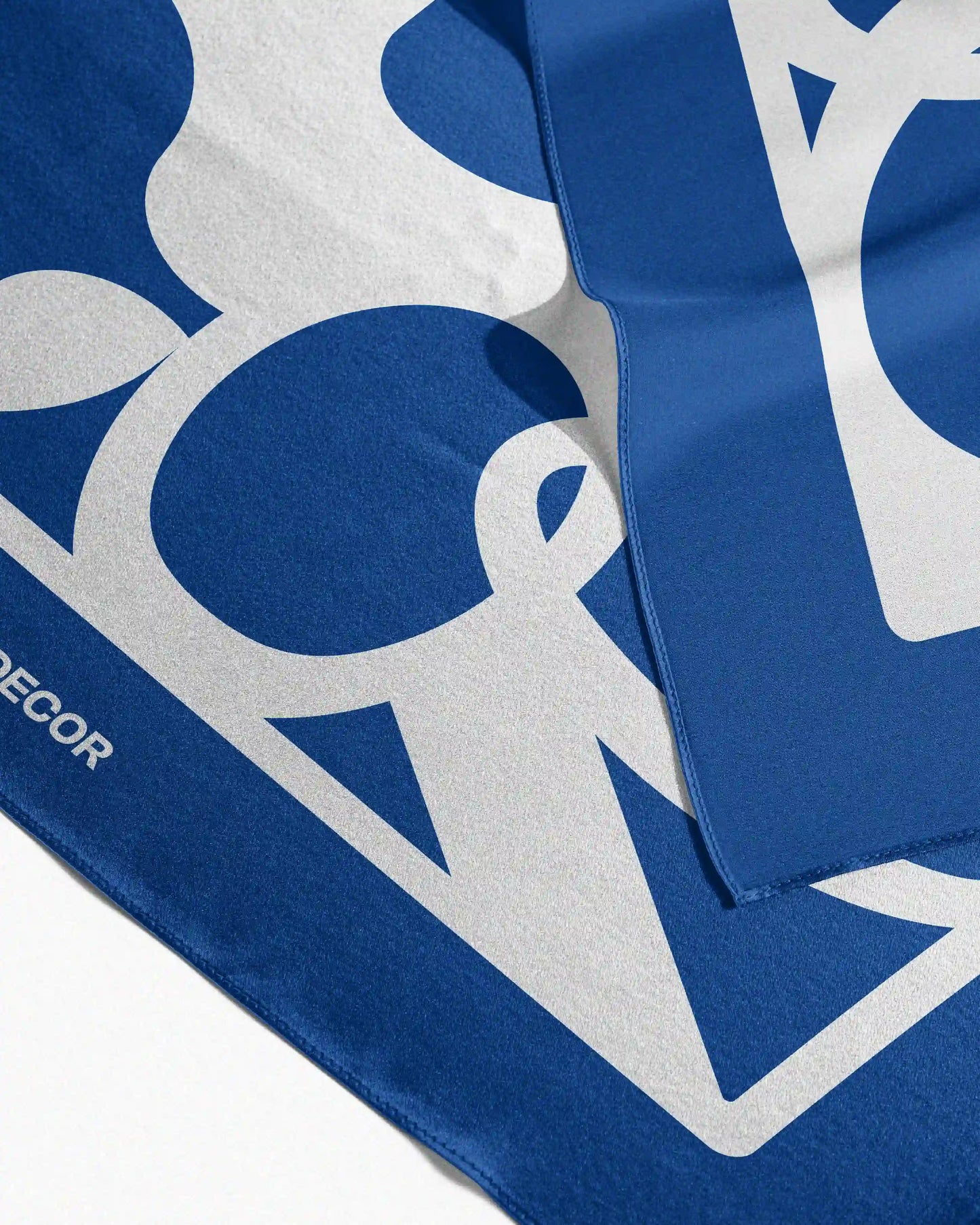 This versatile Klein blue and cream white mulberry silk scarf is neatly folded on a beige background, showcasing its precise edge binding, feature NOOKDECOR's logo frame like design, perfect for use as a sophisticated waist scarf, bandana, handkerchief, twilly, or placemat.