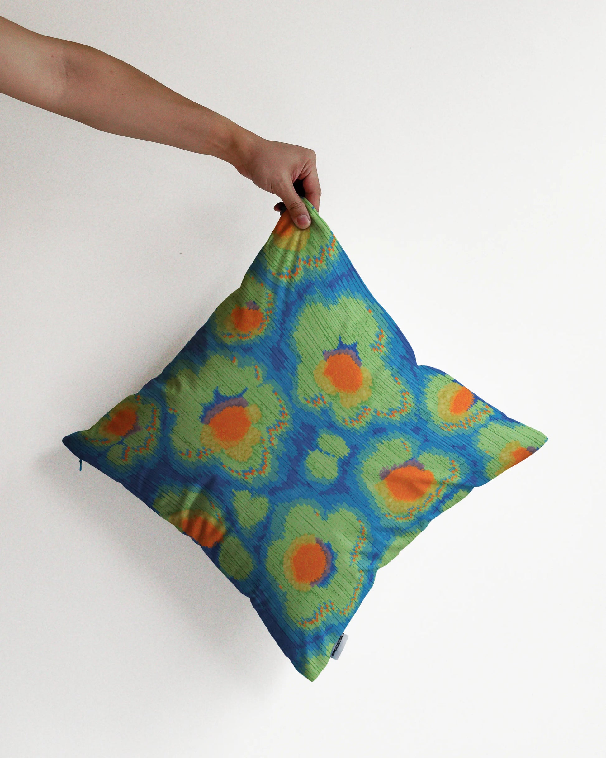 A hand holding an unique abstract floral and leopard cushion cover in green, blue, and orange hues, against a minimalist beige background, perfect for eclectic dopamine decor in a maximalist modern apartment.