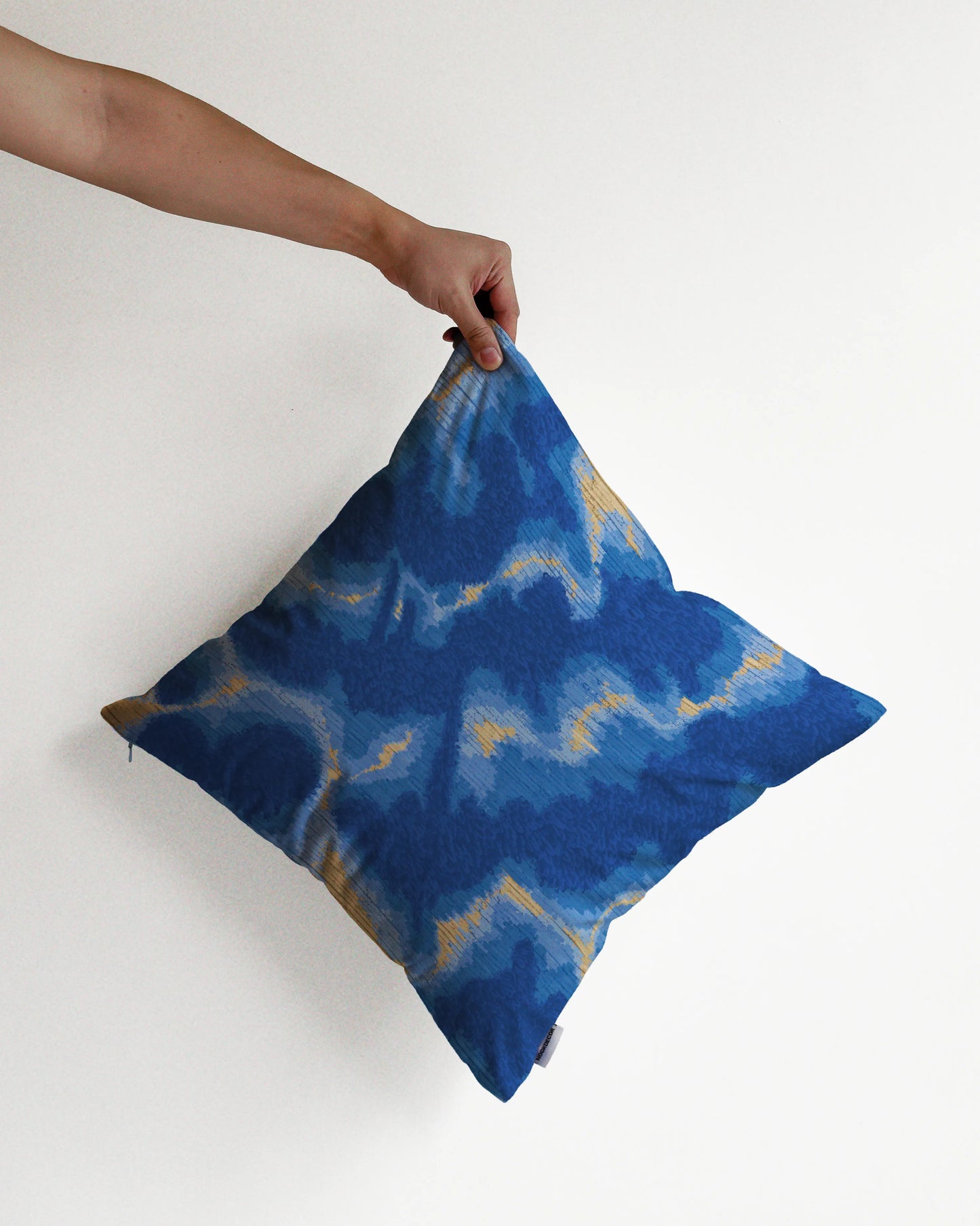 A hand holding a bold abstract hand painted tie dyed cushion cover in Klein blue and sand beige against a minimalist beige background, perfect for eclectic dopamine decor in a modern apartment.