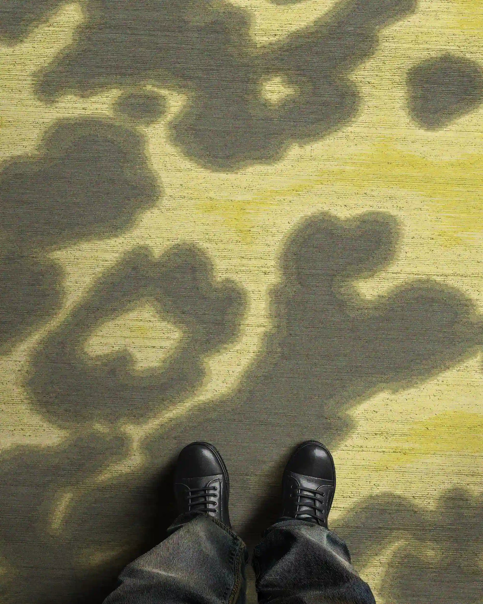A man in trendy baggy jeans and black leather shoes stands on a faux wool, 3mm low pile height cowhide rug featuring abstract floral patterns in grey khaki and light yellow hues, radiating a contemporary vibe in a stylish setting.