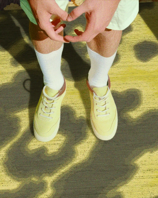 A man in trendy mint green shorts and yellow shoes stands on a faux wool 3mm low pile height cowhide area rug featuring abstract floral patterns in grey khaki and light yellow hues, radiating a contemporary vibe in a stylish setting.
