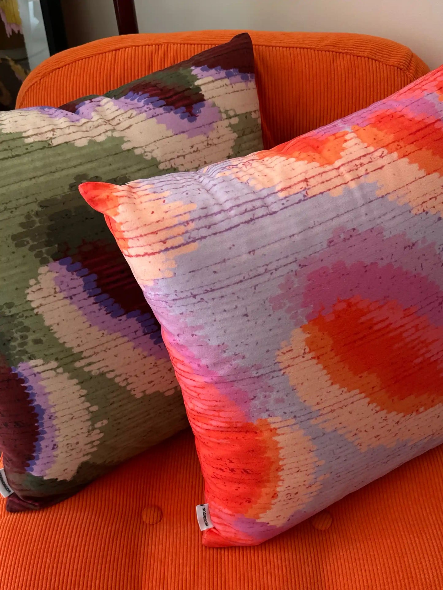 Colorful patterned cushion cover in red, purple and green on an orange couch, in dopamine home. Eclectic decor for maximalist home.