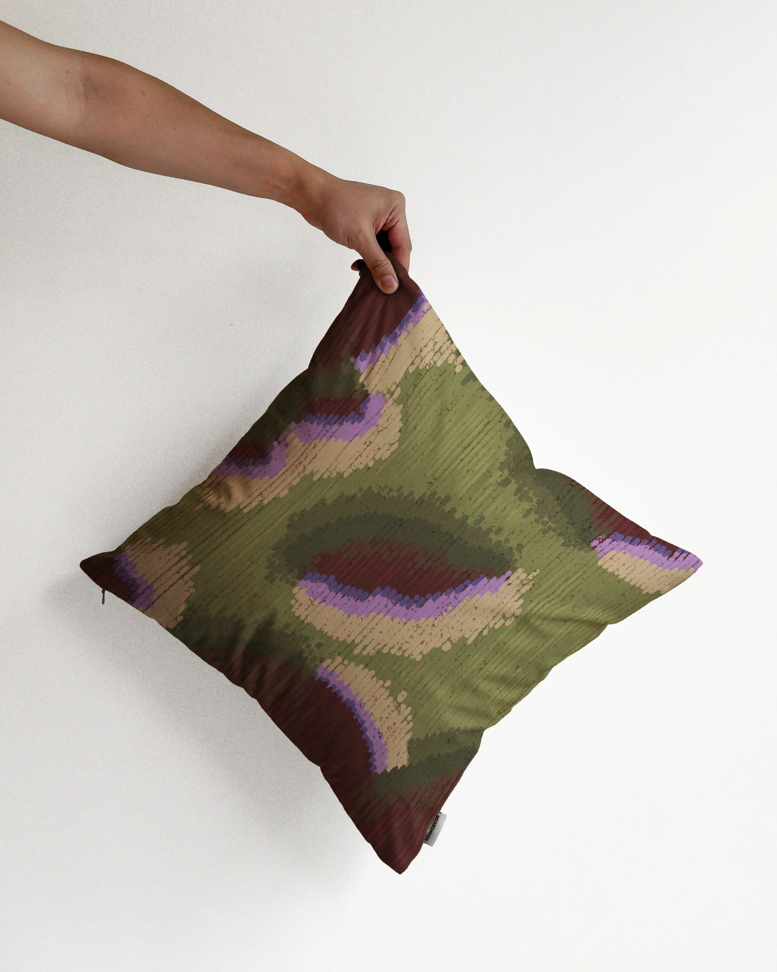 A hand holding a fall vibe, abstract camouflage cushion cover in olive green and burgundy hues, against a minimalist beige background, perfect for eclectic dopamine decor in a modern apartment.
