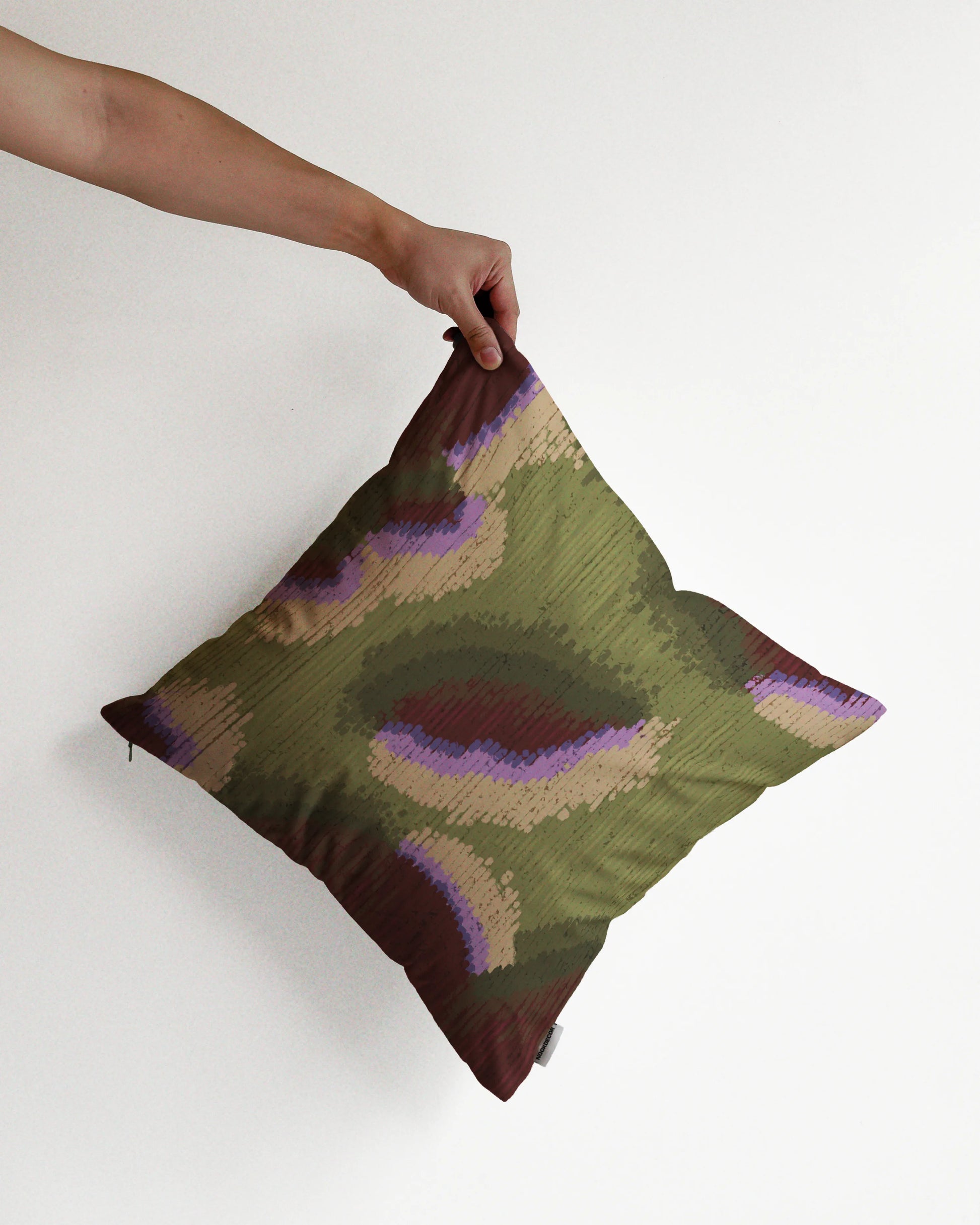 A hand holding a fall vibe, abstract camouflage cushion cover in olive green and burgundy hues, against a minimalist beige background, perfect for eclectic dopamine decor in a modern apartment.
