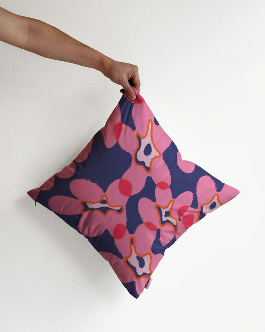 A hand holding an unique abstract floral cushion cover in pink and dark blue hues, against a minimalist beige background, perfect for eclectic dopamine decor in a modern apartment.