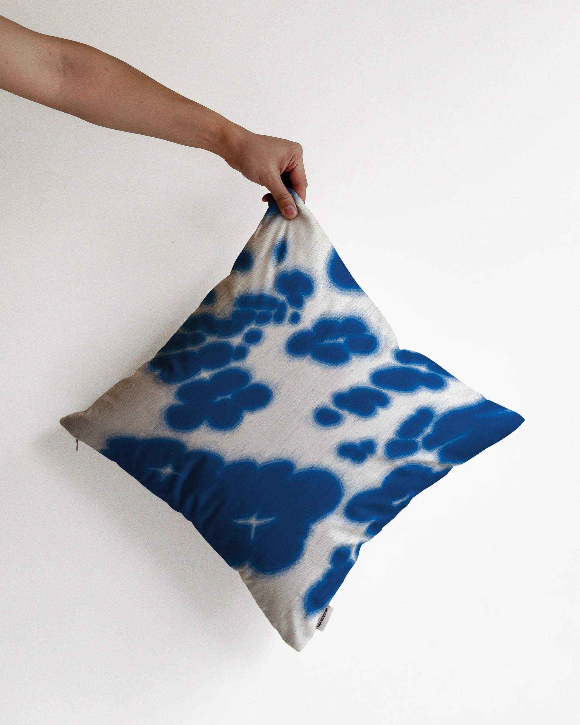 A hand holding a bold, abstract floral and cowhide cushion cover in Klein blue and off white hues, against a minimalist beige background, perfect for eclectic dopamine decor in a modern apartment.