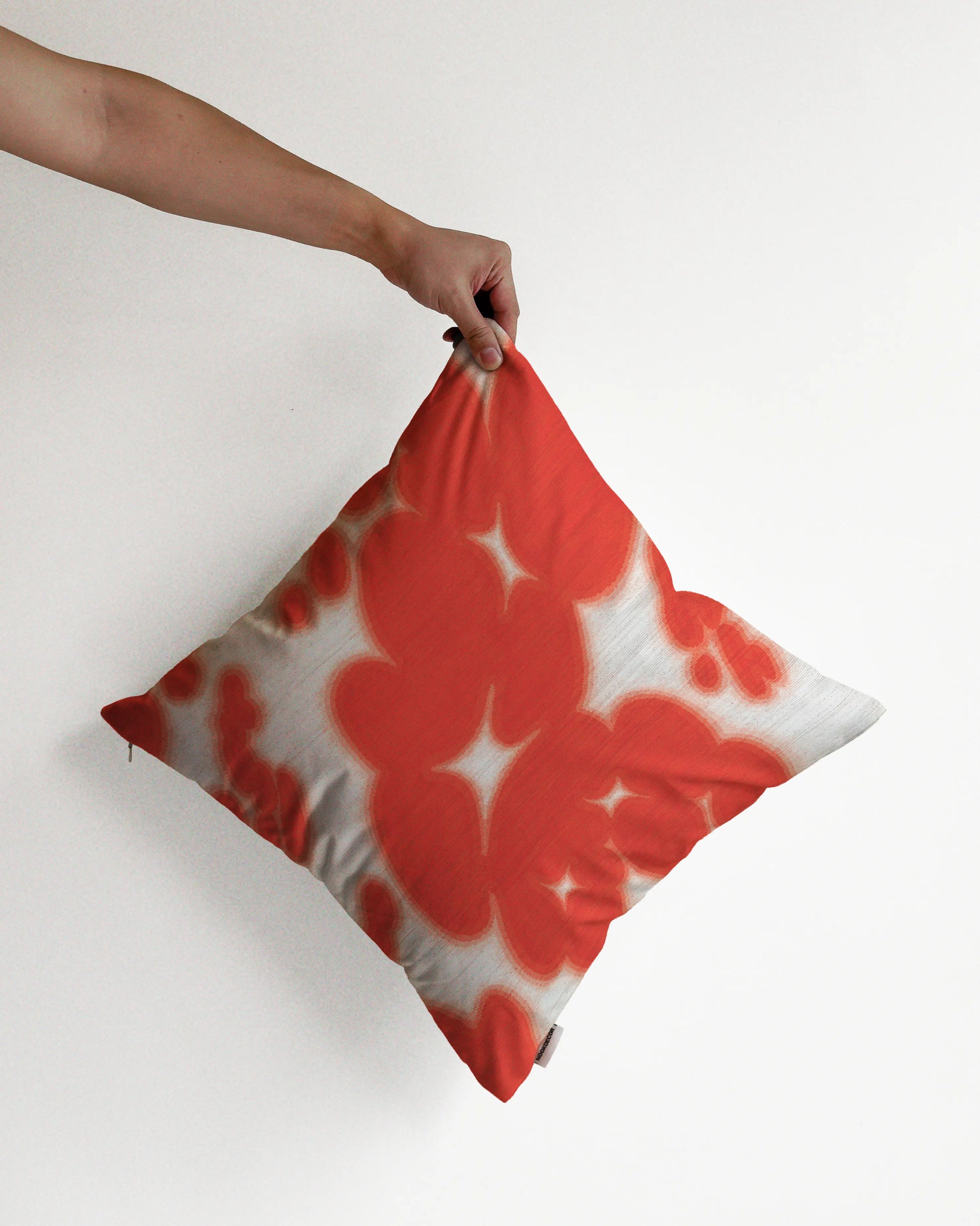 A hand holding a bold, abstract floral and cowhide cushion cover in red and off white hues, against a minimalist beige background, perfect for eclectic dopamine decor in a modern apartment.