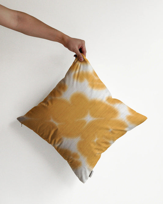 A hand holding a bold, abstract floral and cowhide cushion cover in yellow and off white hues, against a minimalist beige background, perfect for eclectic dopamine decor in a modern apartment.