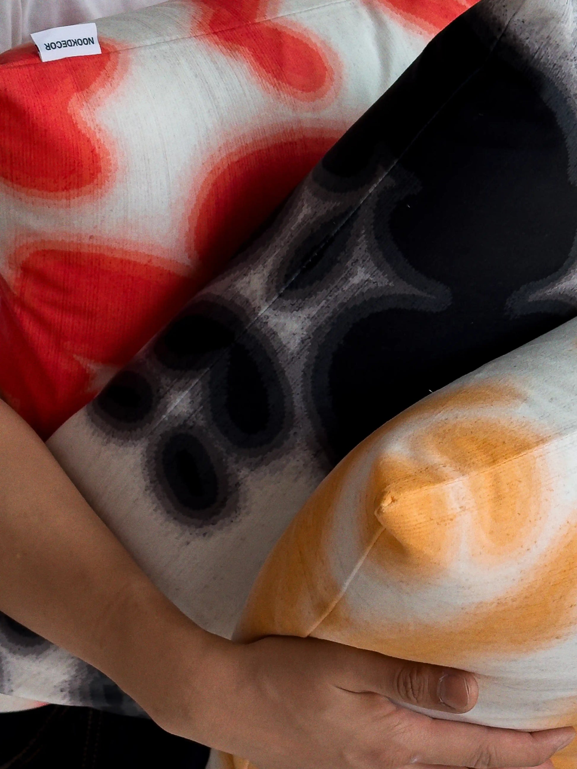 Hand holding a set of three coordinating abstract cowhide floral cushion covers, showing mix of abstract cowhide and floral patterns for bold dopamine sofa styling.
