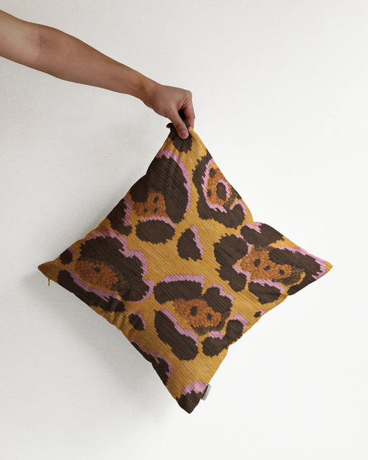 A hand holding a bold abstract floral and leopard cushion cover in yellow, pink and brown hues, against a minimalist beige background, perfect for eclectic dopamine decor in a maximalist modern apartment.