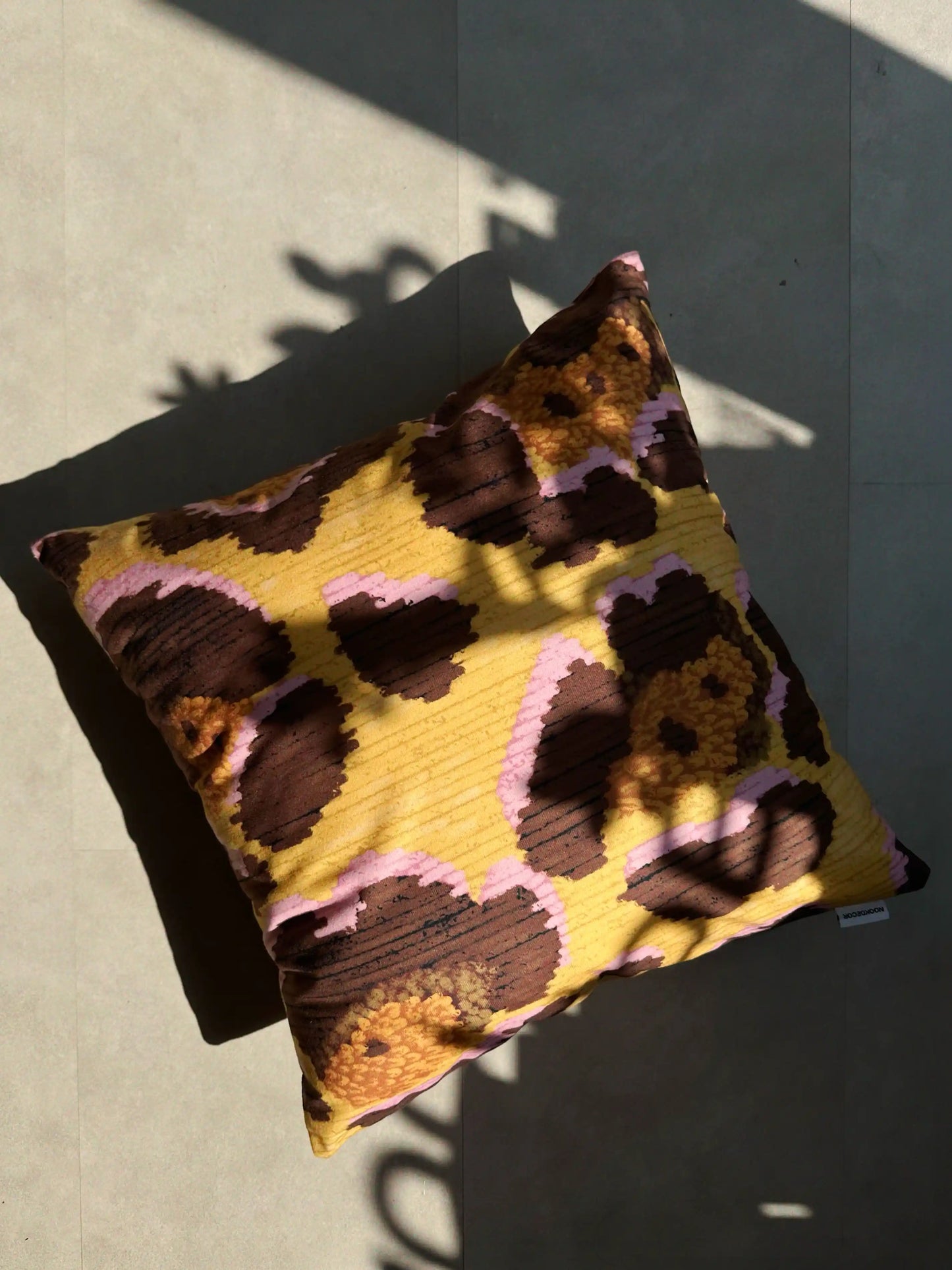 Throw pillow with a floral leopard pattern in yellow, brown and pink on the floor in a sunlit room. Dopamine home decor cushion cover for eclectic apartment.