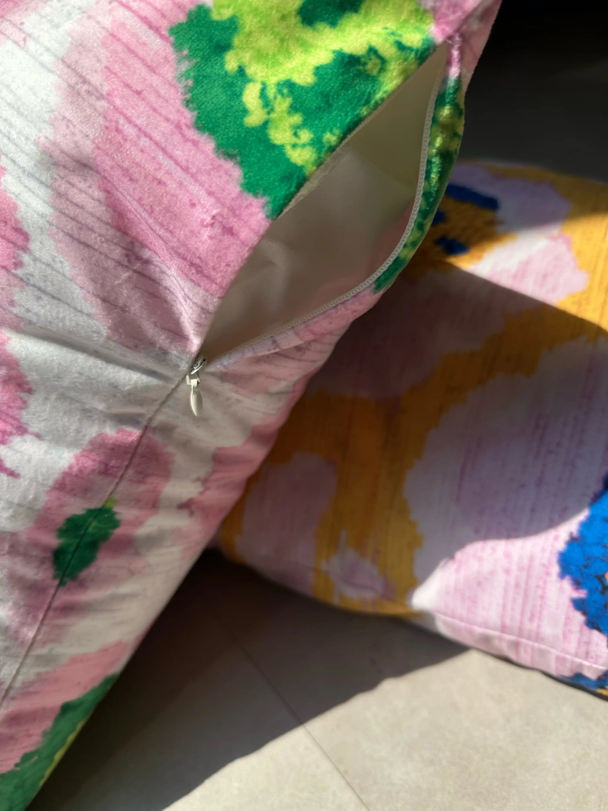 Close up detail of a colorful pink and green floral leopard cushion with hidden zipper details on the floor, with its other color, purple and yellow, underneath.