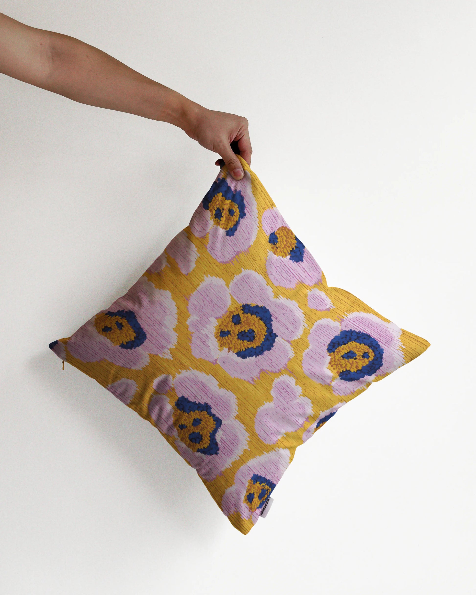 A hand holding a bold abstract floral and leopard cushion cover in yellow, pastel purple and Klein blue hues, against a minimalist beige background, perfect for eclectic dopamine decor in a maximalist modern apartment.