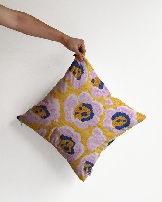 A hand holding a bold abstract floral and leopard cushion cover in yellow, pastel purple and Klein blue hues, against a minimalist beige background, perfect for eclectic dopamine decor in a maximalist modern apartment.