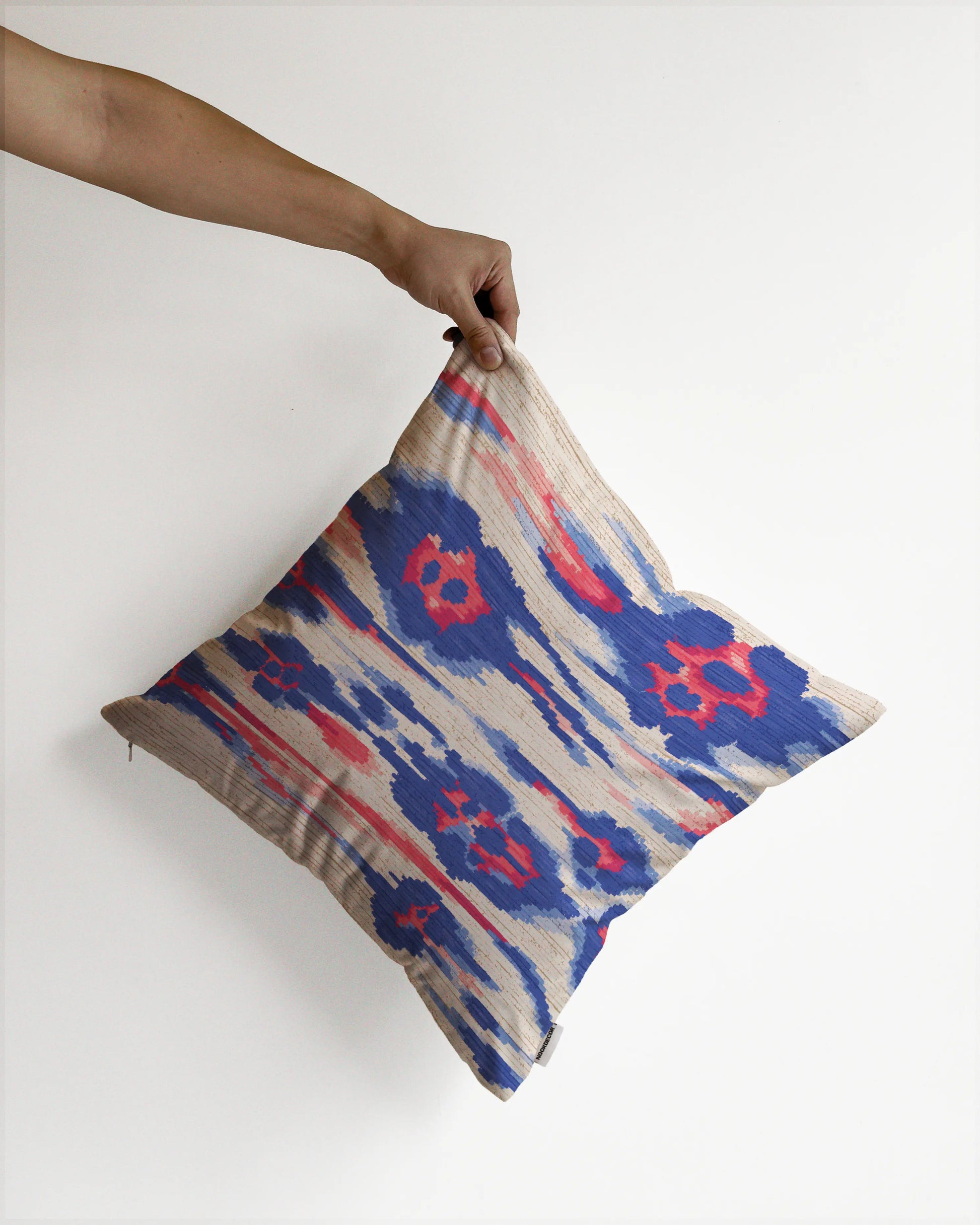 A hand holding an eclectic abstract floral and leopard cushion cover in red, blue and off white hues, against a minimalist beige background, perfect for dopamine decor in a maximalist modern apartment.