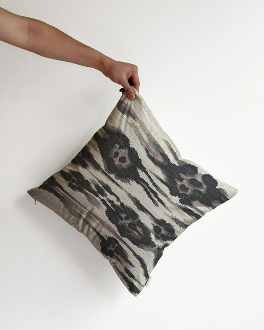 A hand holding an eclectic abstract floral and leopard cushion cover in dark grey and off white hues with slight touch of pink, green and purple touch, against a minimalist beige background, perfect for dopamine home decor in a maximalist modern house.