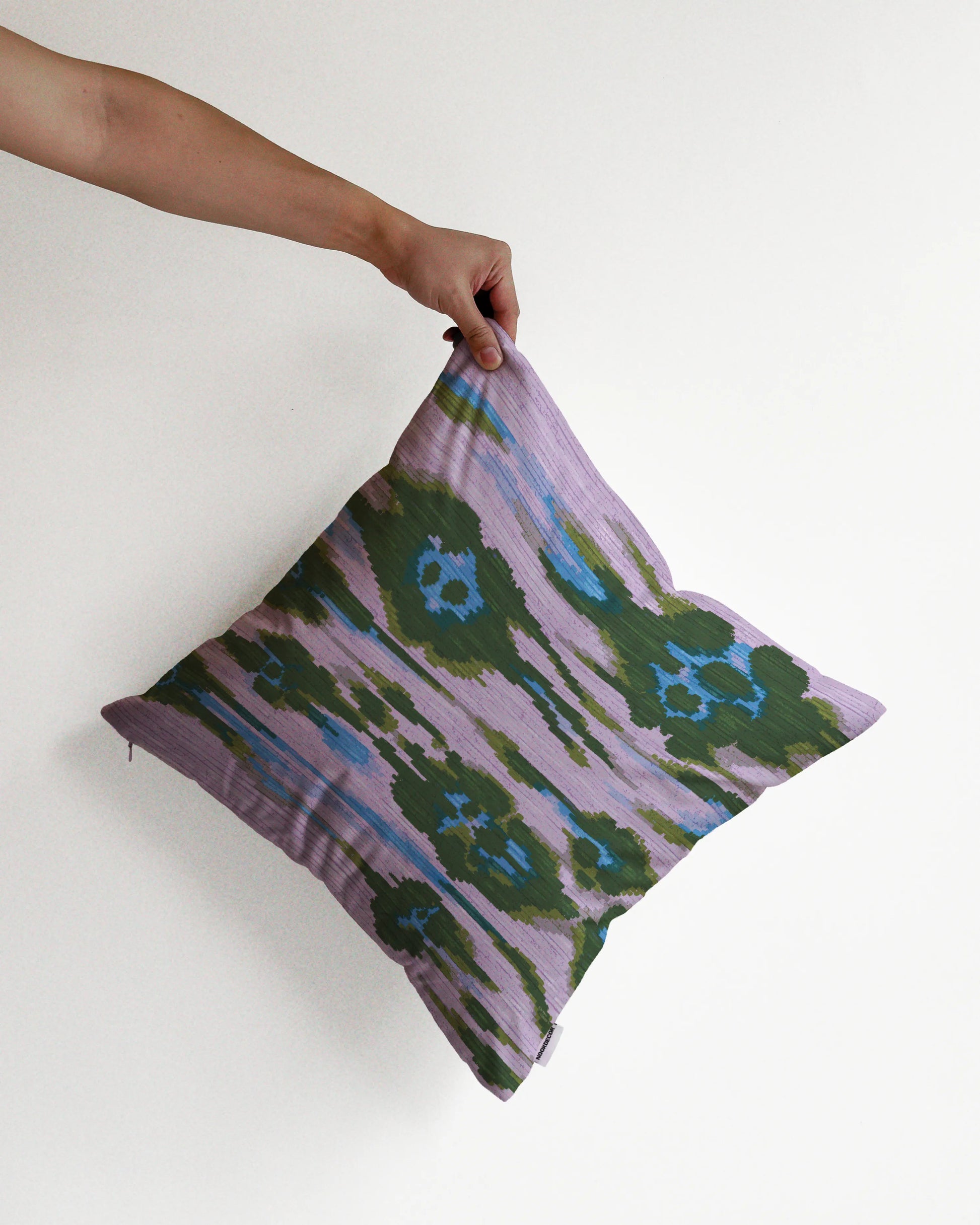 A hand holding an eclectic abstract floral and leopard cushion cover in purple, blue and deep green hues, against a minimalist beige background, perfect for dopamine decor in a maximalist home.