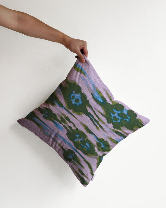 A hand holding an eclectic abstract floral and leopard cushion cover in purple, blue and deep green hues, against a minimalist beige background, perfect for dopamine decor in a maximalist home.
