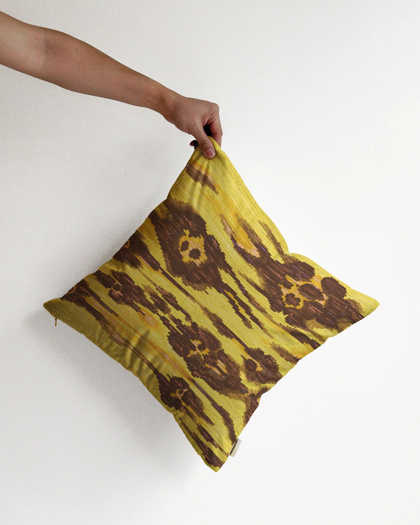 A hand holding an eclectic abstract floral and leopard cushion cover in yellow and brown hues, against a minimalist beige background, perfect for dopamine home decor in a maximalist modern house.