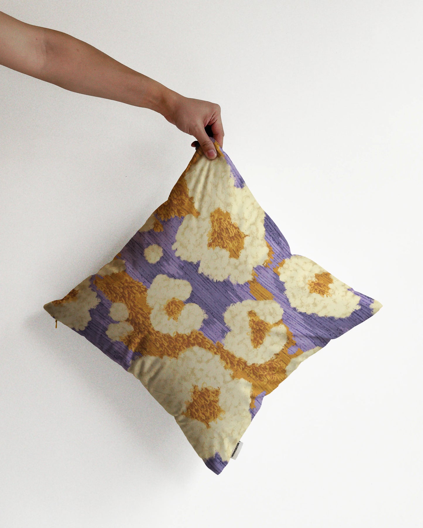 A hand holding an eclectic abstract floral and leopard, pop corn like cushion cover in purple, mustard yellow and creamy beige hues, against a minimalist beige background, perfect for dopamine home decor in a maximalist modern apartment.